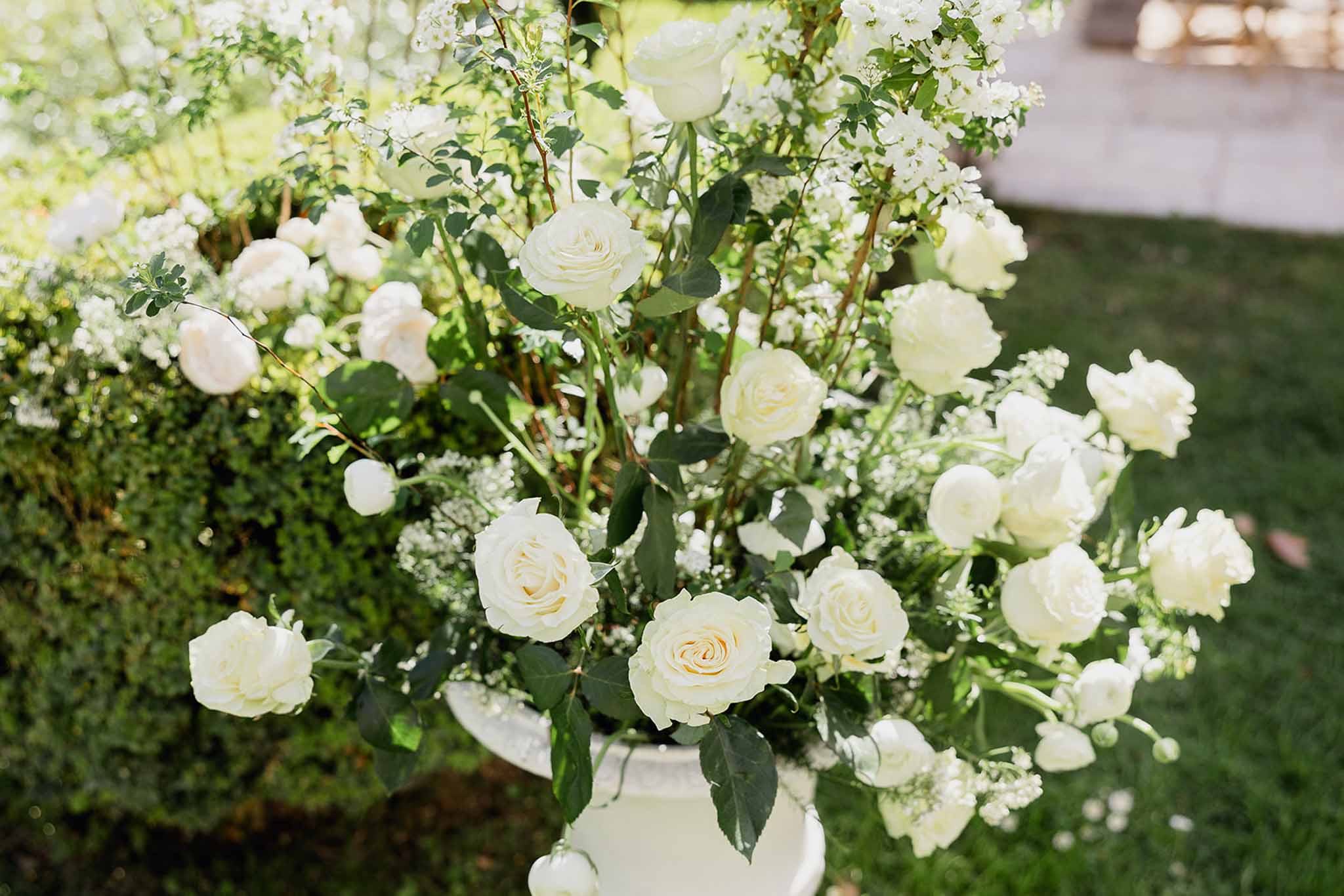 Ivory and peach rose floral arrangement with baby's breath in white vase at outdoor garden wedding