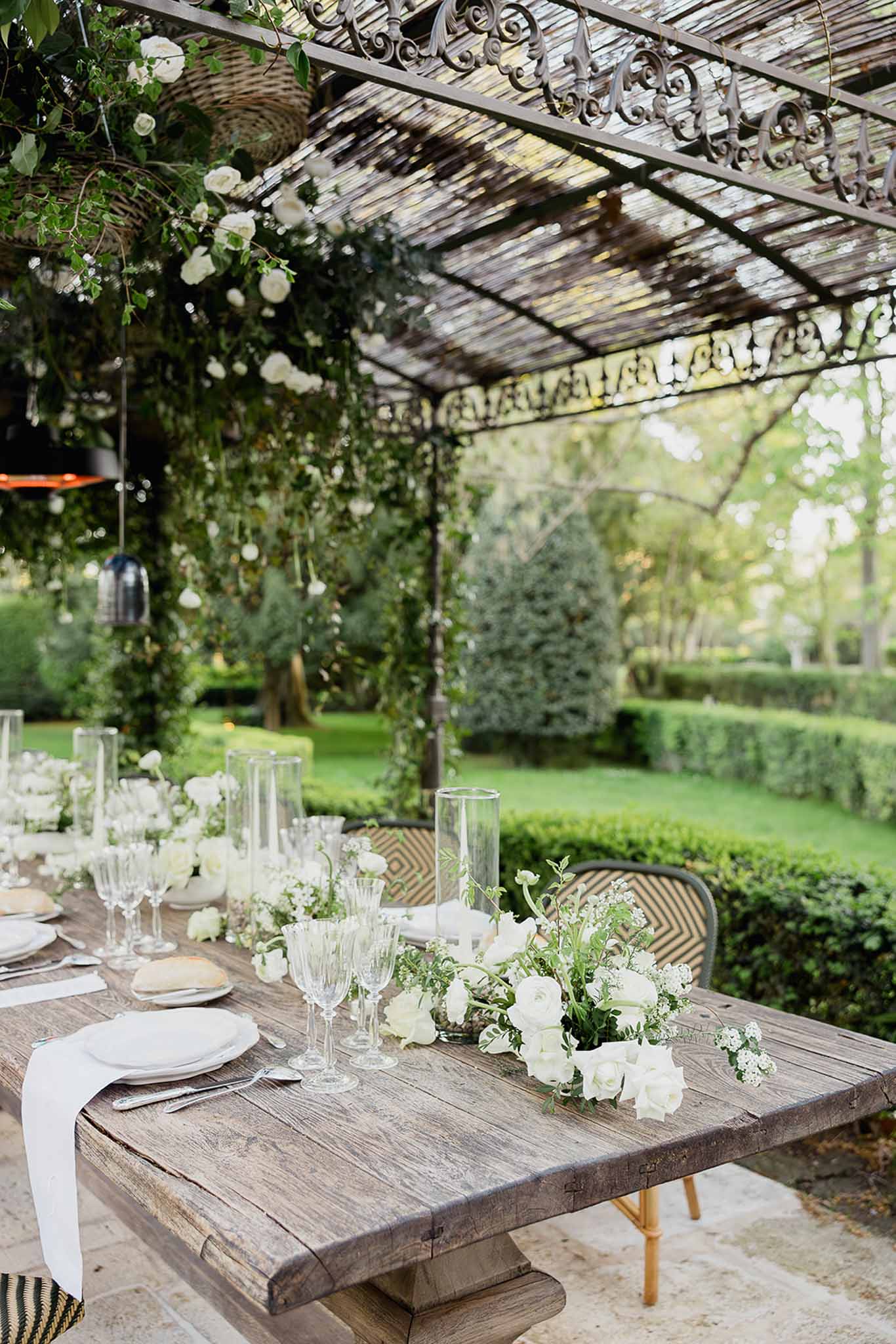 Outdoor reception table setting under pergola with white florals at garden venue
