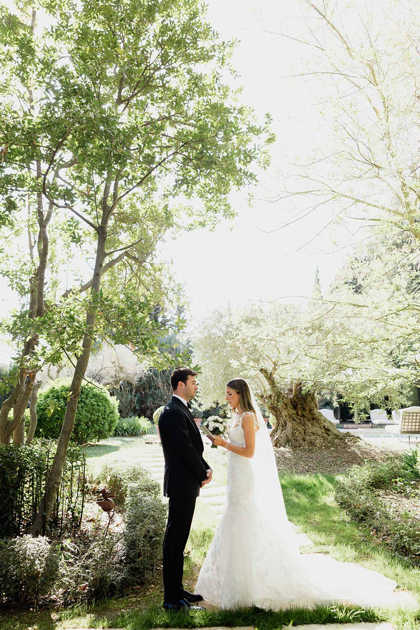 Bride and groom posing together in elegant garden pathway with mature trees and manicured landscaping