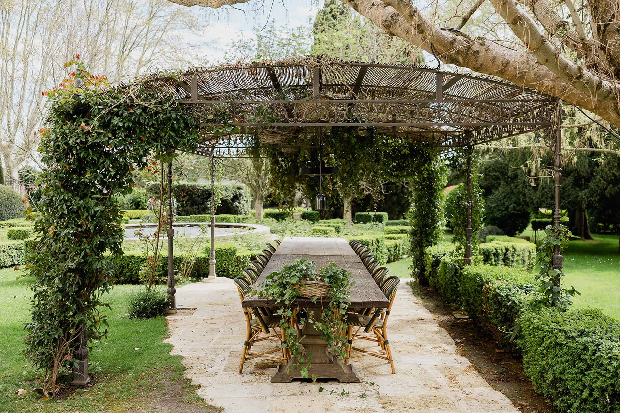 Long wooden dining table under ivy-covered pergola in estate garden venue