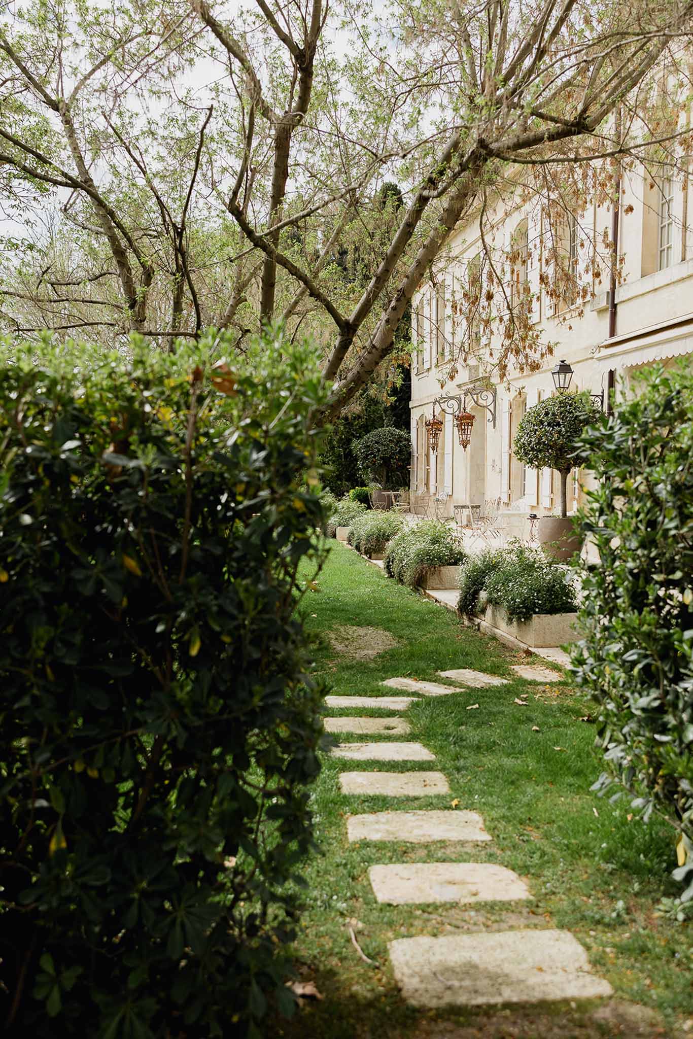 Garden pathway leading to cream stone villa with ivy facade and formal landscaping