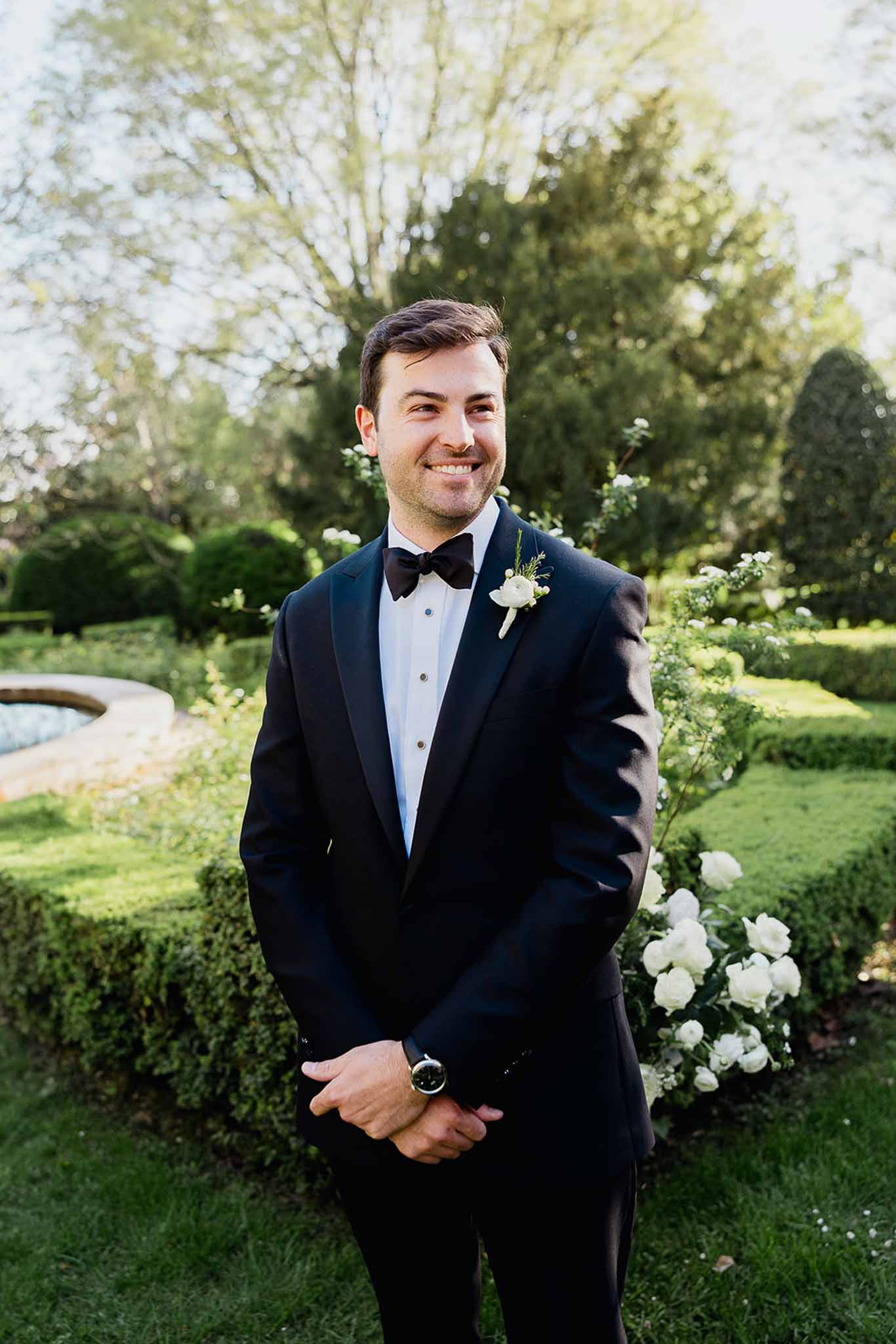 Groom in black tuxedo portrait in manicured garden setting