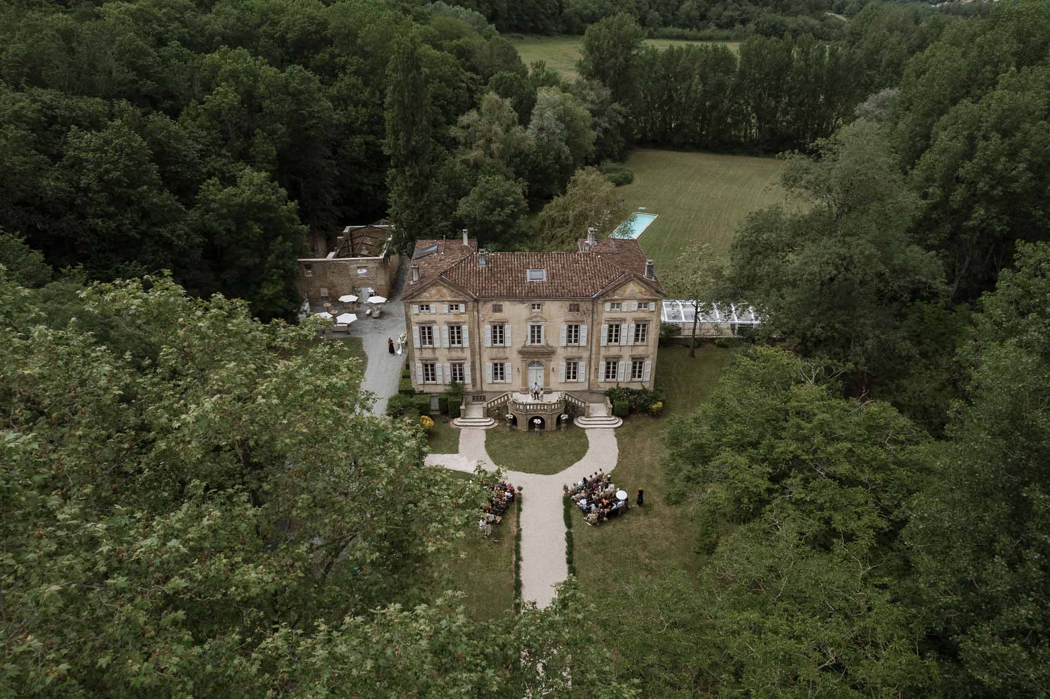 Aerial view of outdoor wedding ceremony at stone château with guests seated on manicured lawn