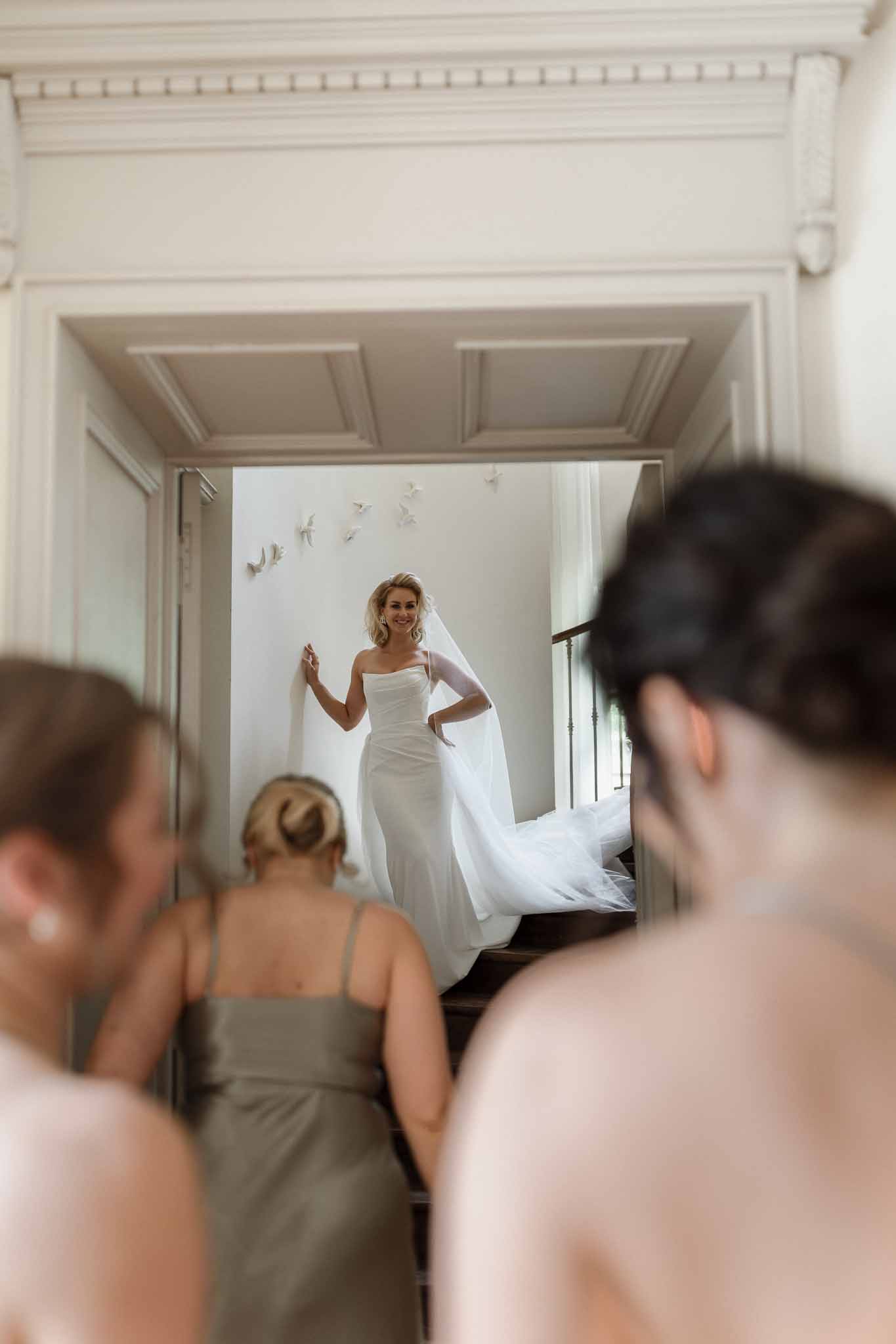 Bride in ivory gown revealing dress to bridesmaids in sage dresses during getting ready moment