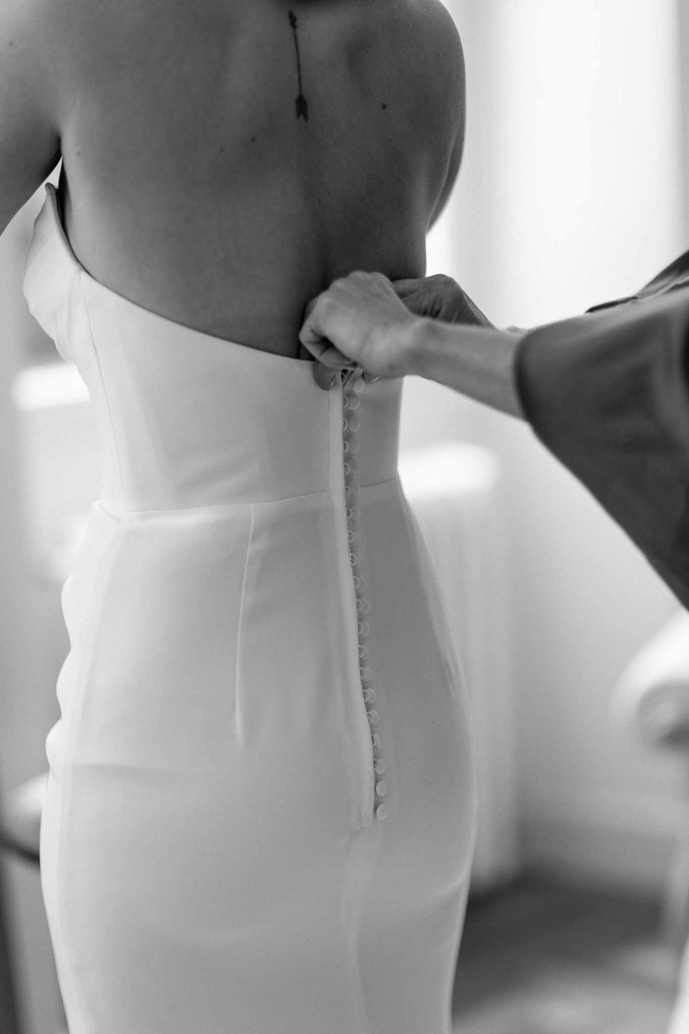 Bride's wedding dress being buttoned during getting ready preparations
