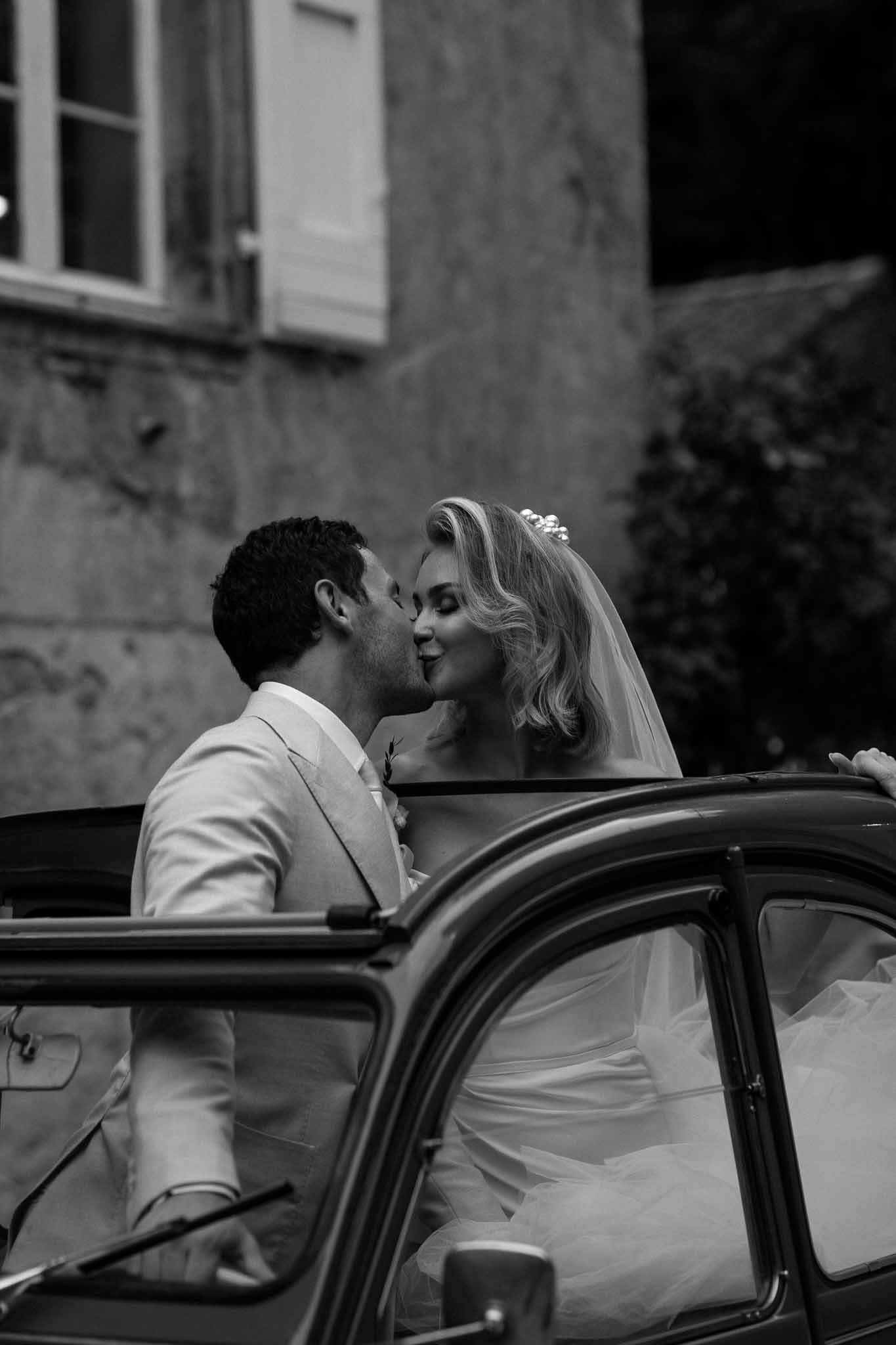 Bride and groom kissing beside vintage car in urban courtyard