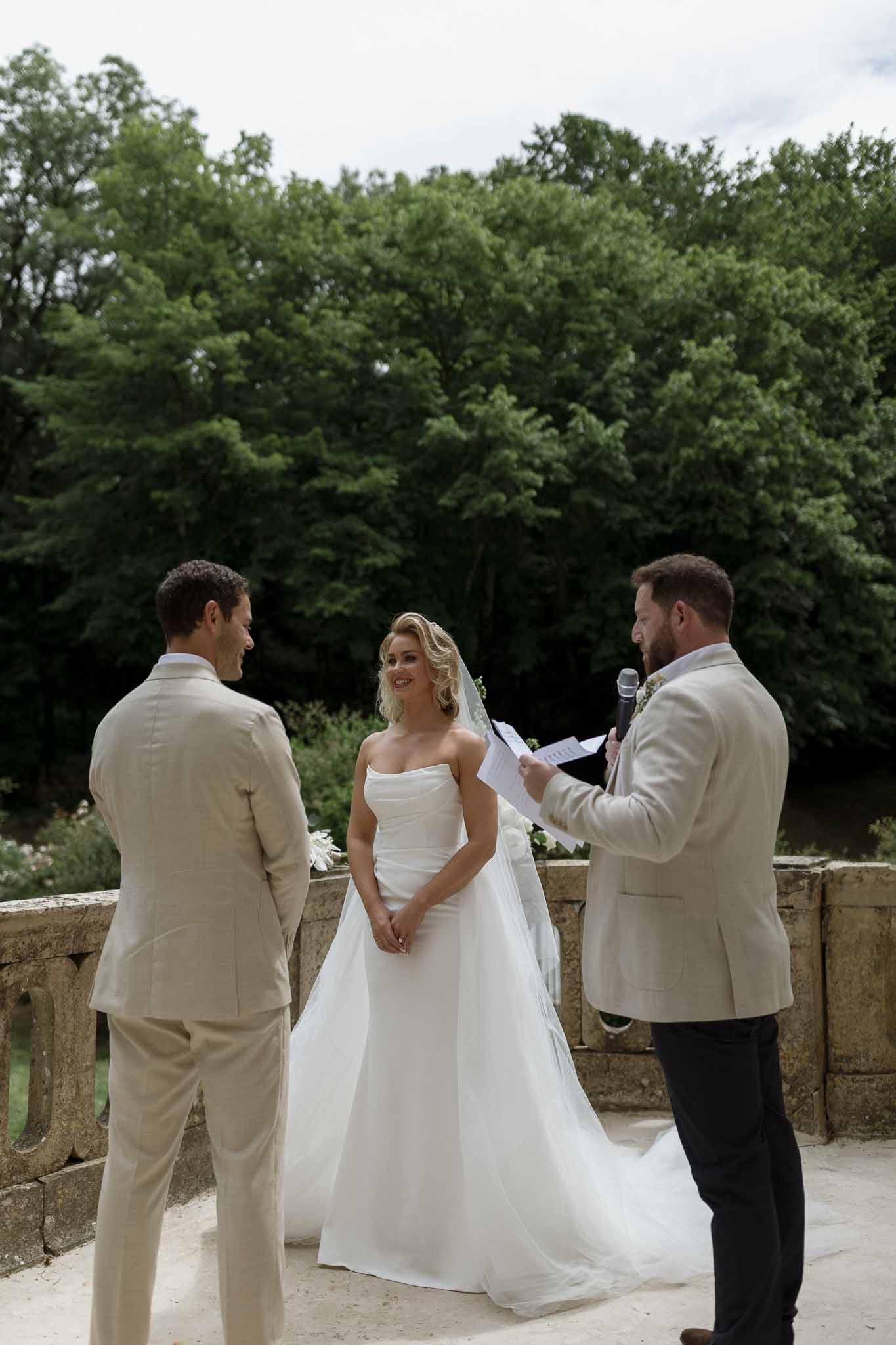 Bride and groom during outdoor ceremony on stone terrace with officiant and forest backdrop