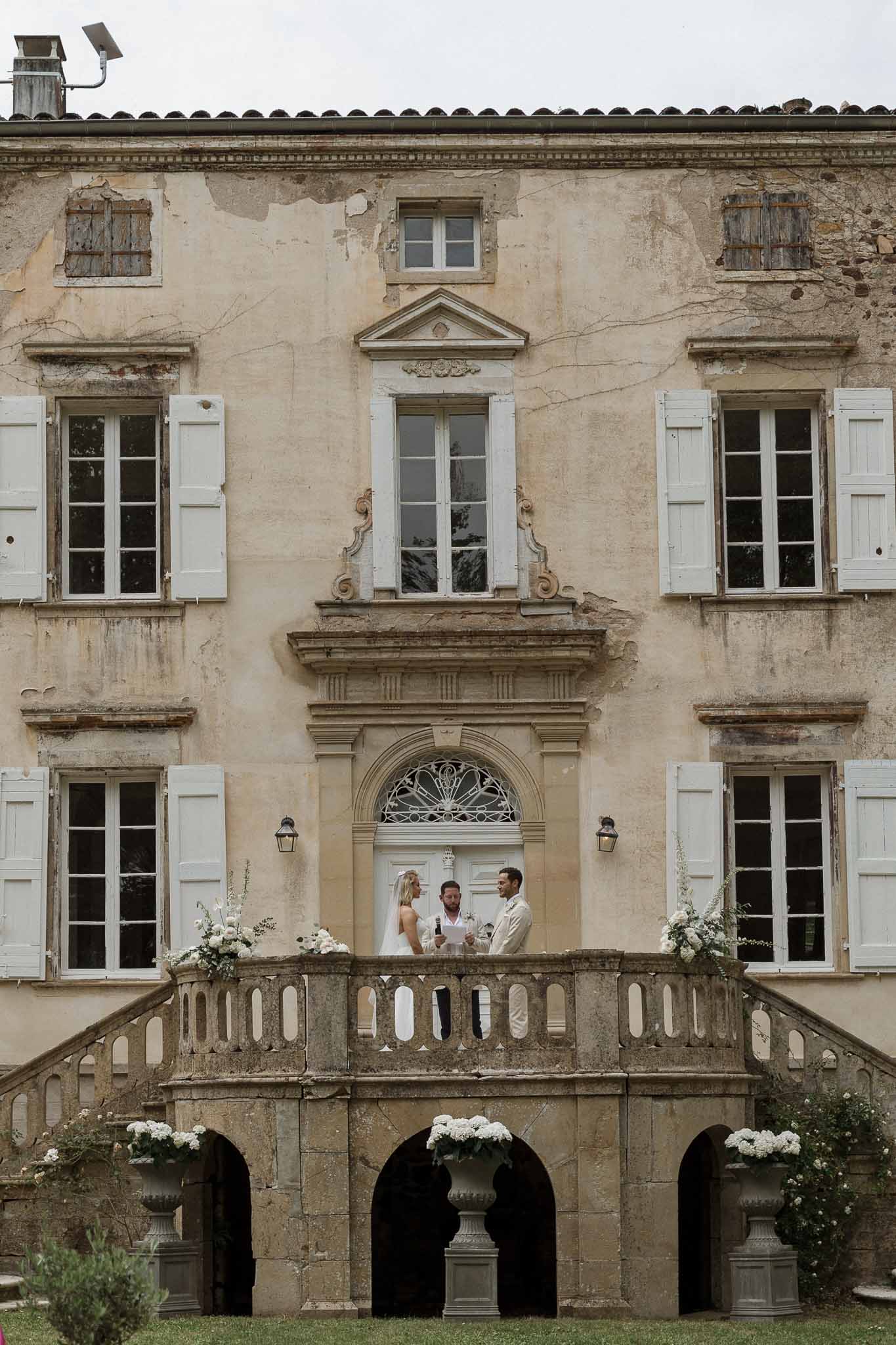 Bride and groom ceremony on stone balcony at historic French château with officiant