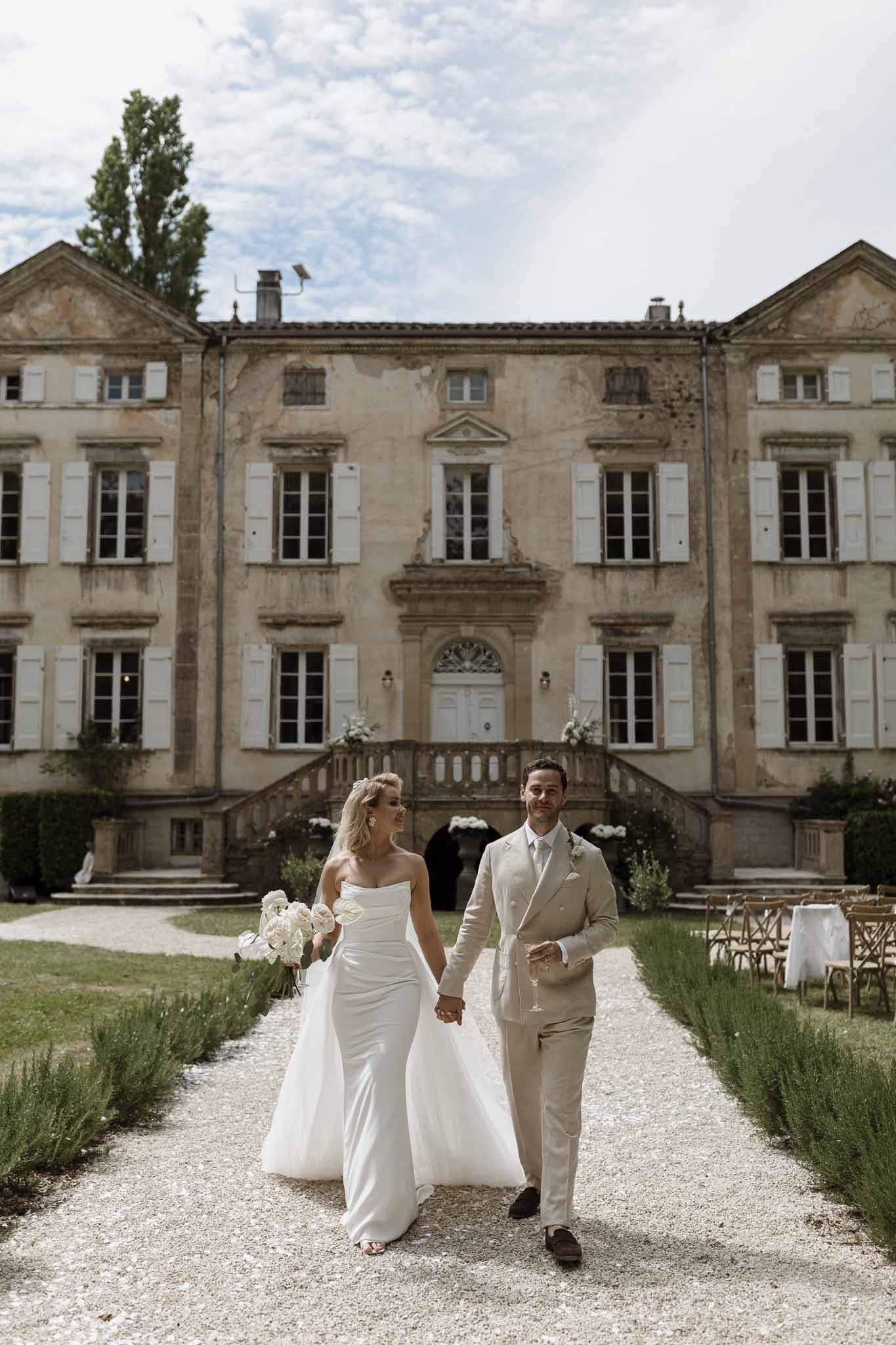 Bride and groom walking hand-in-hand toward historic French château during wedding day