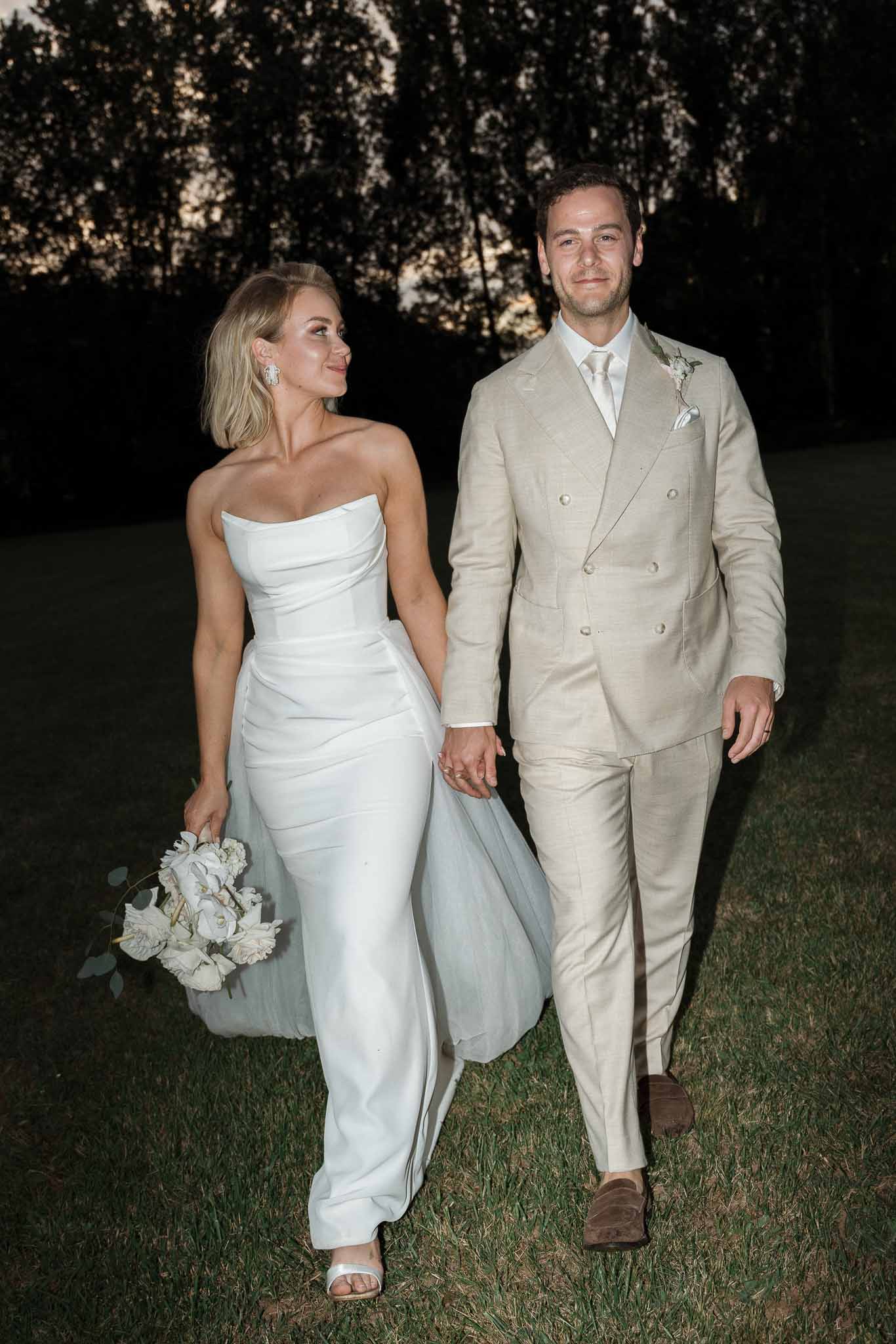 Bride and groom walking together on outdoor lawn at night at garden wedding venue