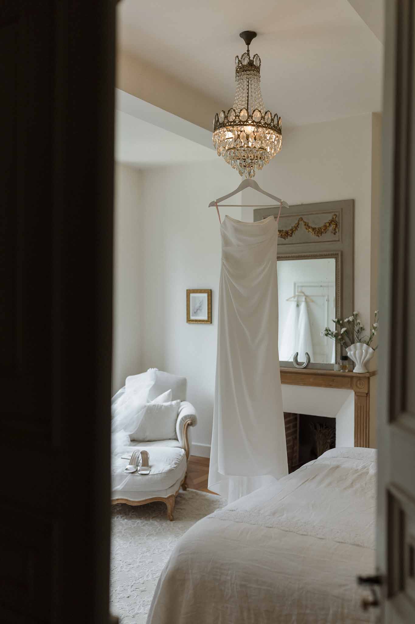 Wedding dress hanging in elegant bridal suite with chandelier and classic European decor