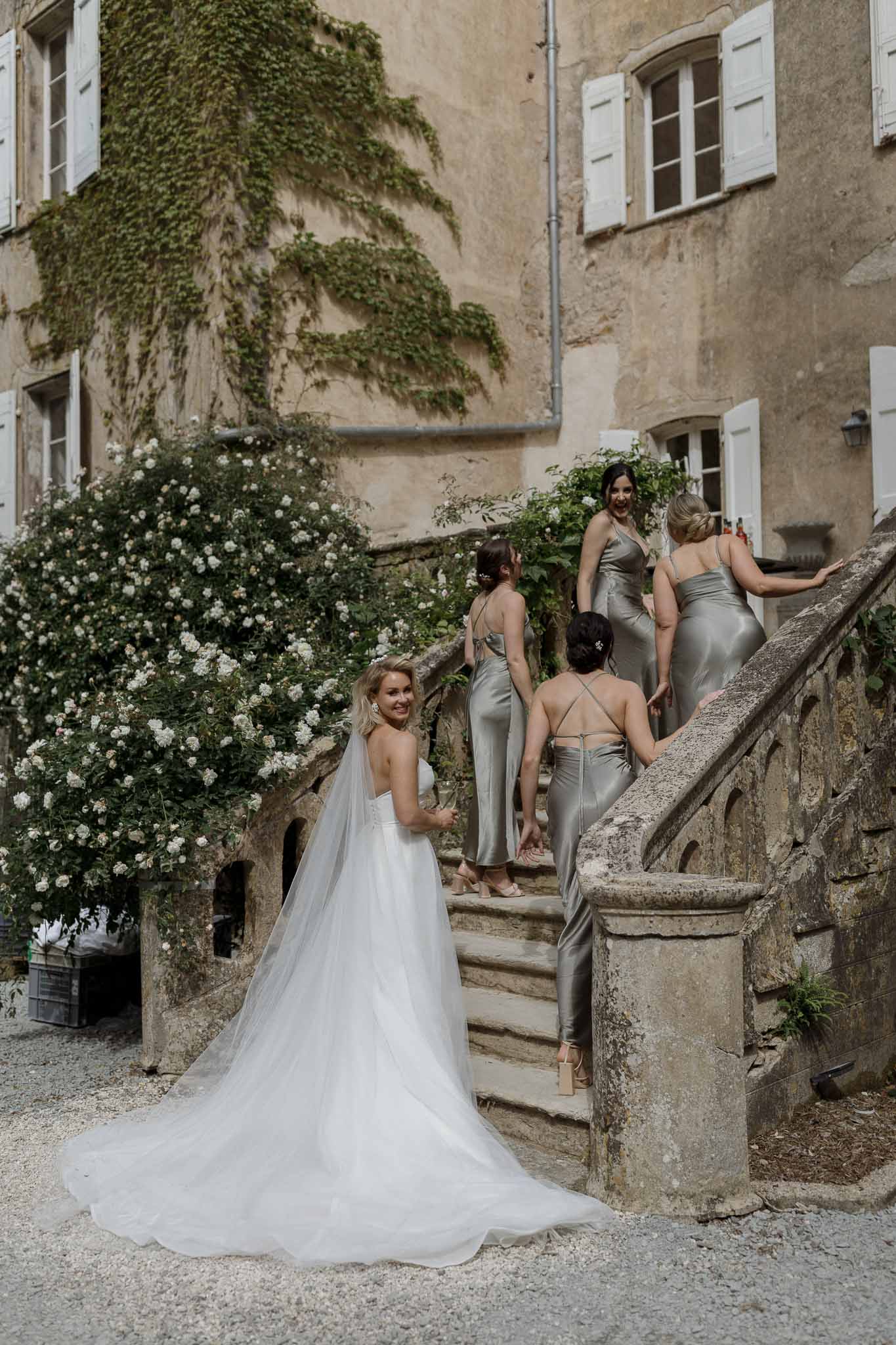 Bride and bridesmaids in sage green dresses at stone courtyard with ivy-covered walls