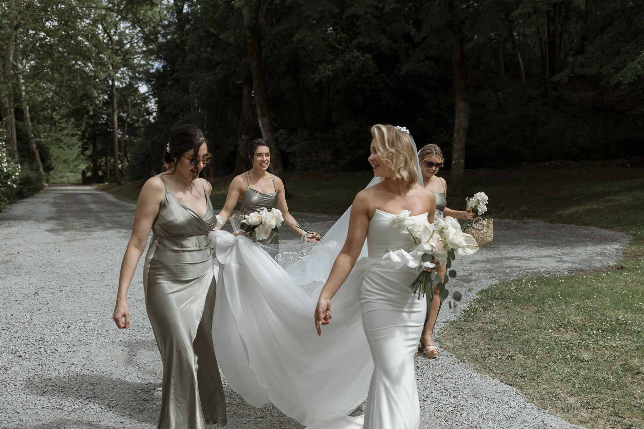 Bride and bridesmaids walking along tree-lined path at outdoor wedding venue