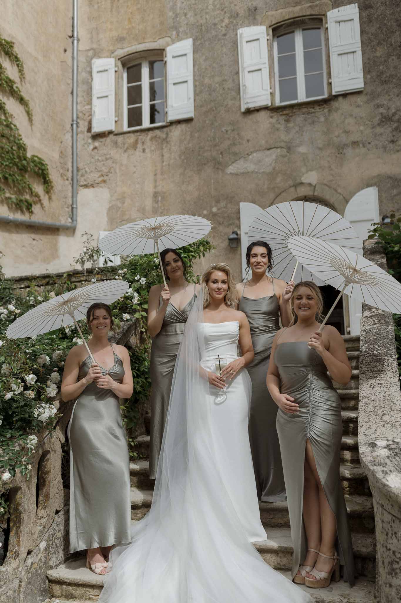 Bridal party with white parasols on stone staircase at European stone building