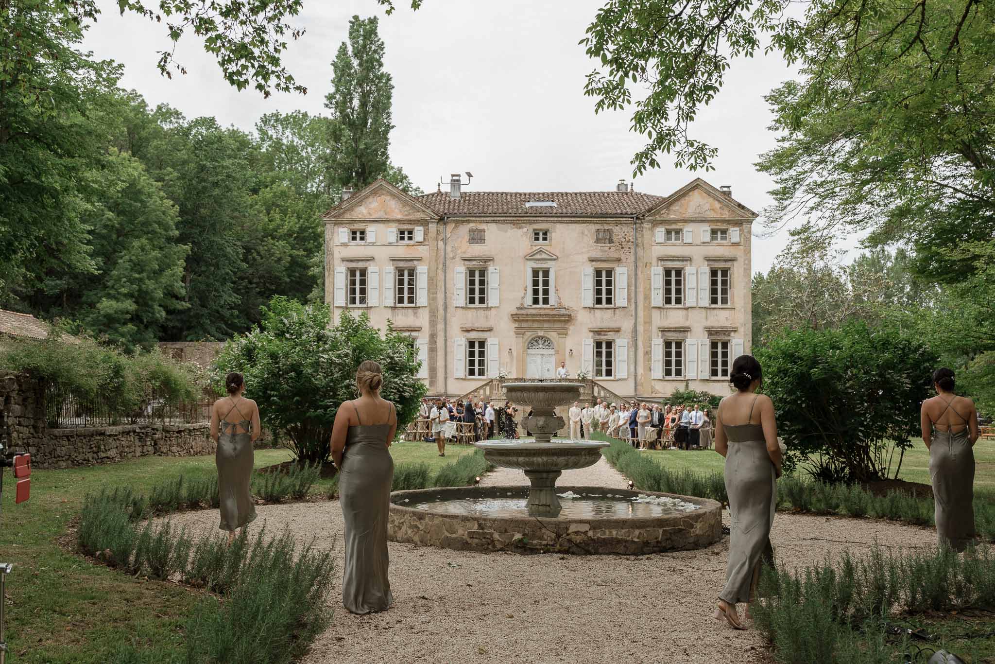 Bridal party in sage green dresses by stone fountain at French château gardens