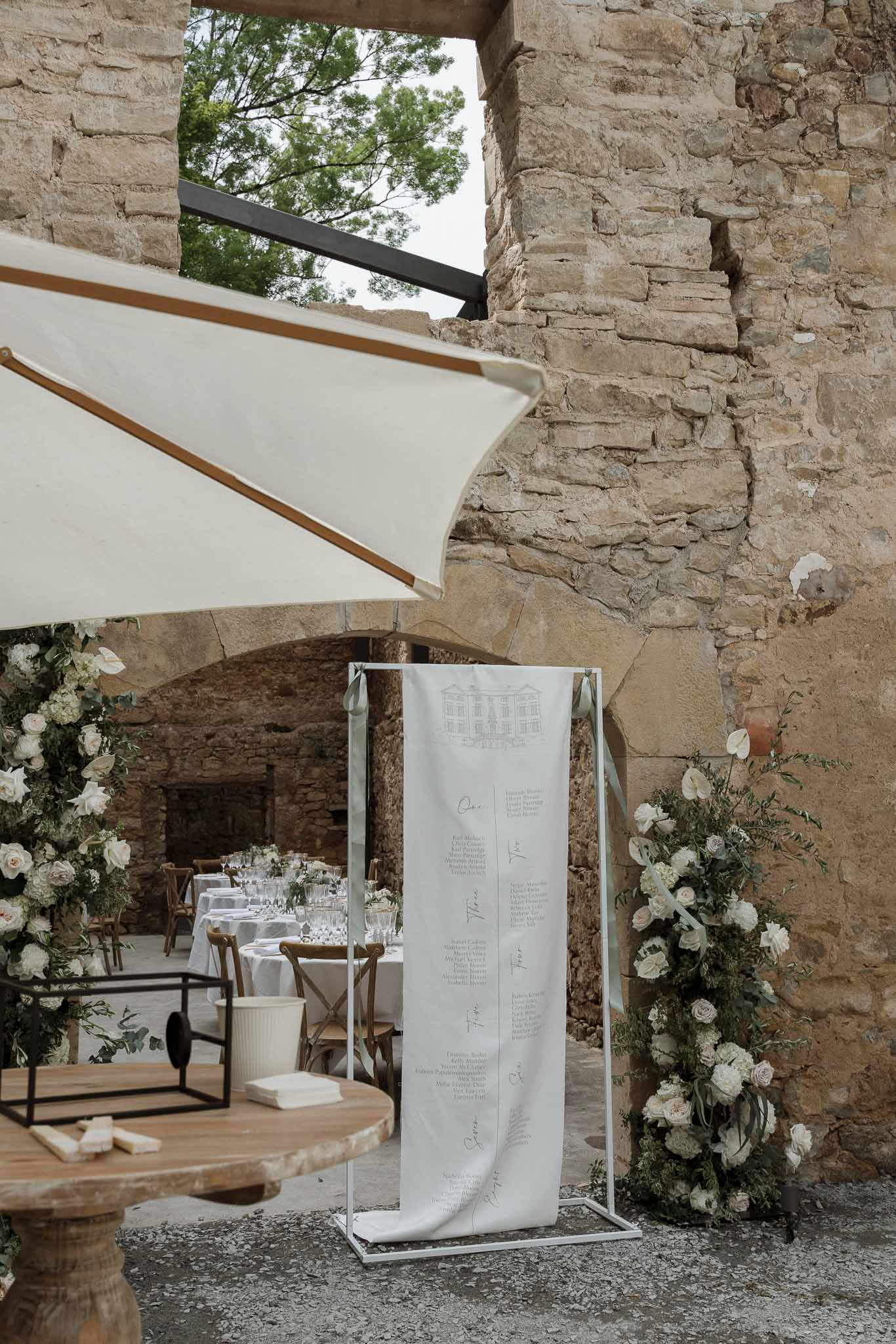 Wedding seating chart display with floral arrangements in stone courtyard reception space