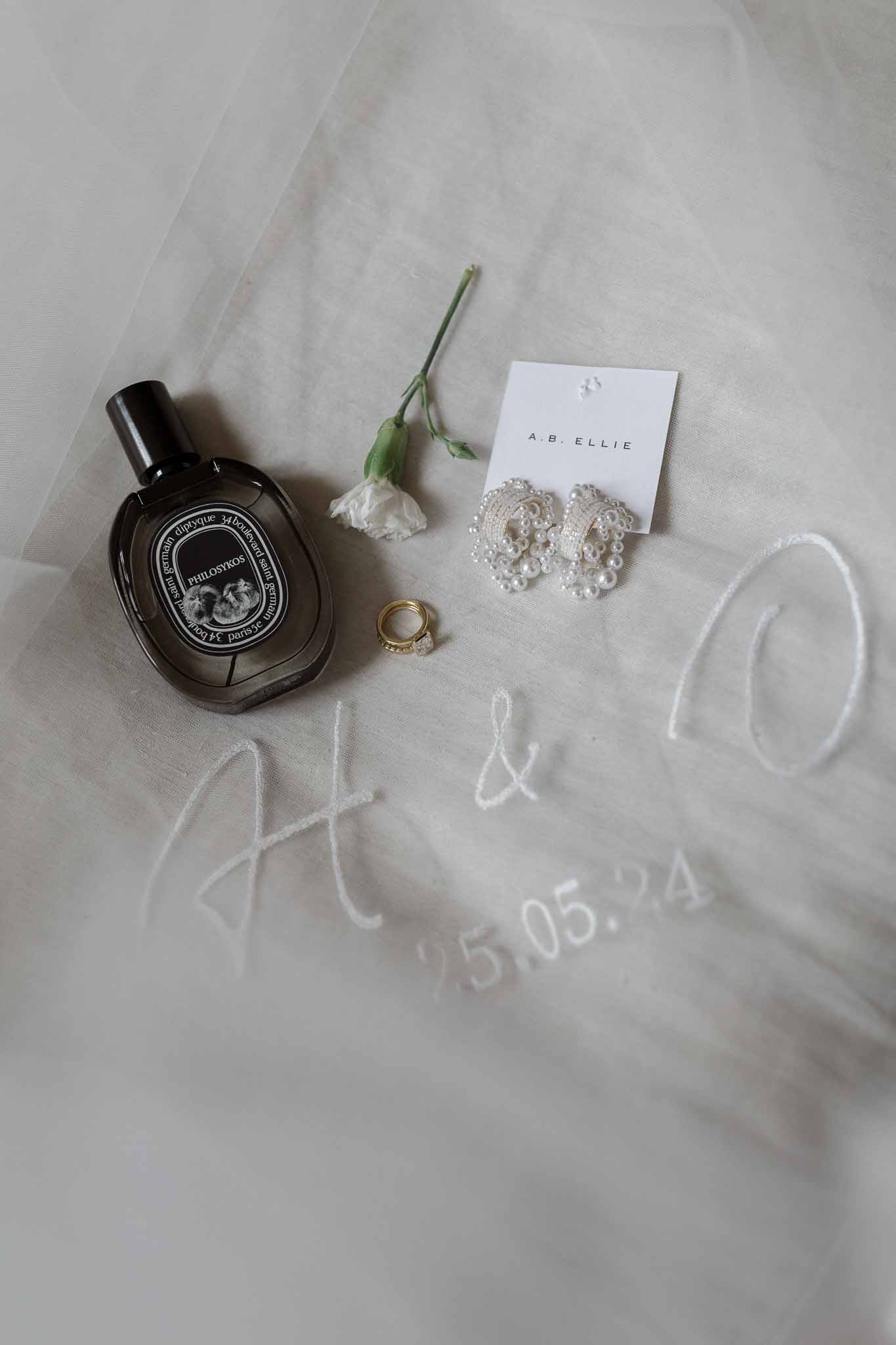 Wedding accessories flat lay with perfume, jewelry and rings on ivory tulle fabric
