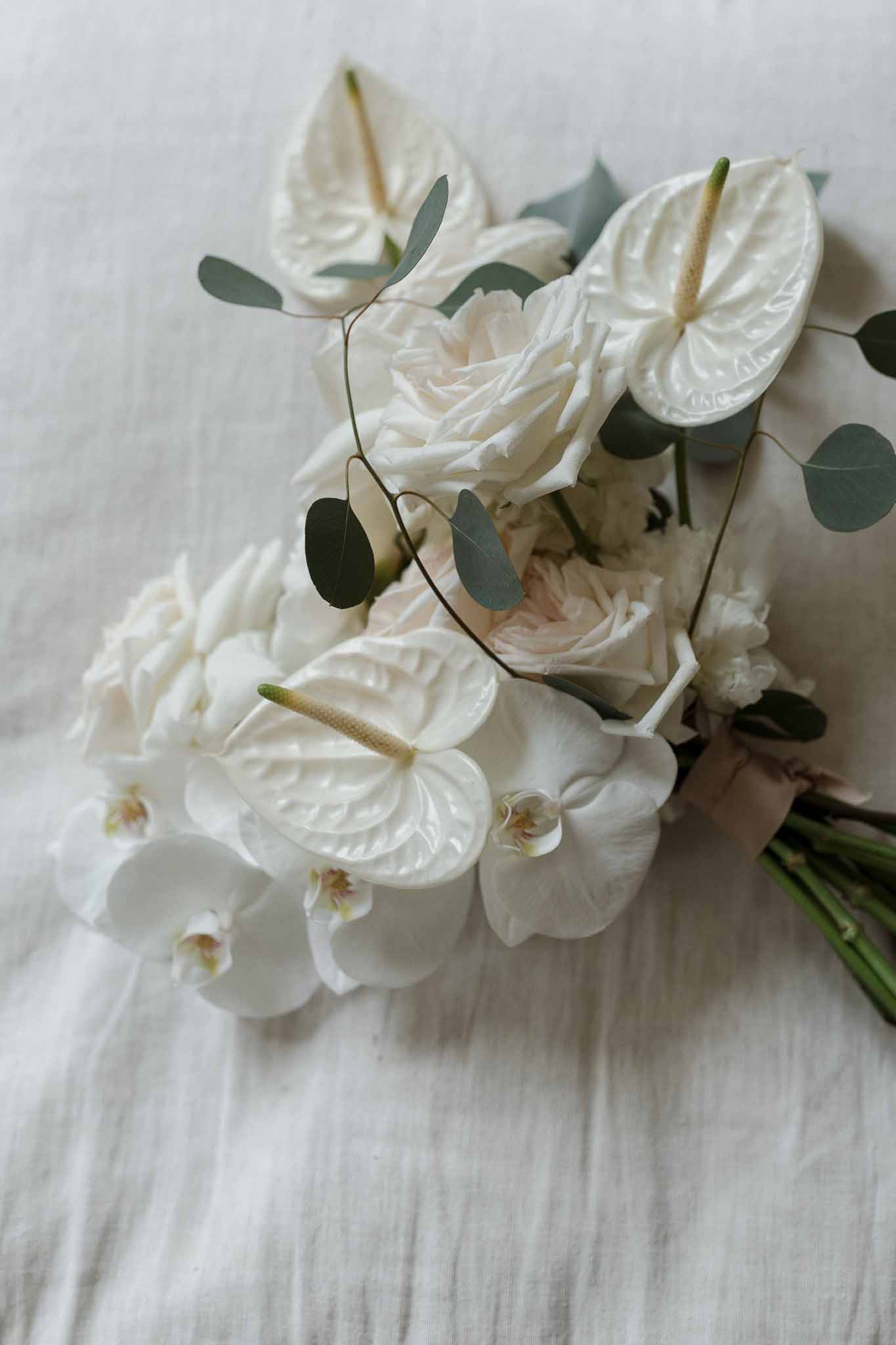 White bridal bouquet with garden roses and orchids arranged on white linen fabric