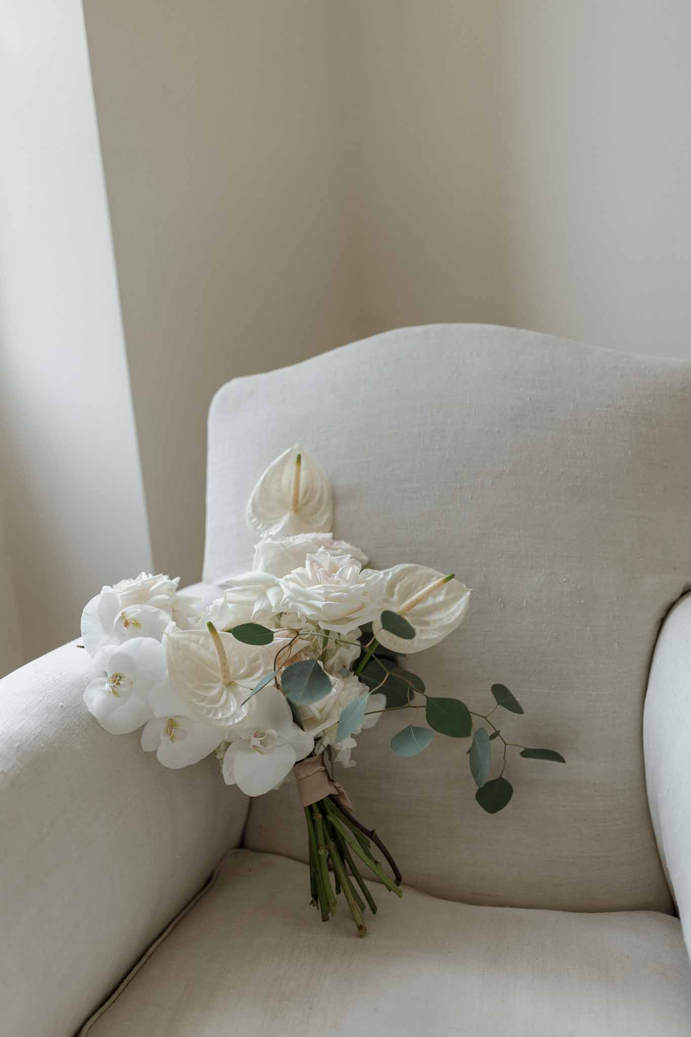 Bridal bouquet with white roses and peonies on cream chair in elegant indoor setting