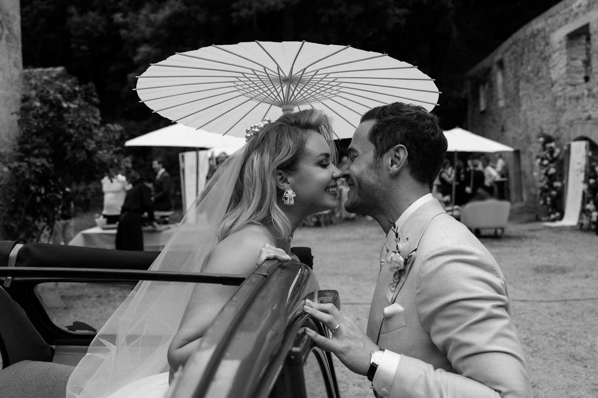 Bride and groom sharing intimate moment in vintage car during outdoor château reception