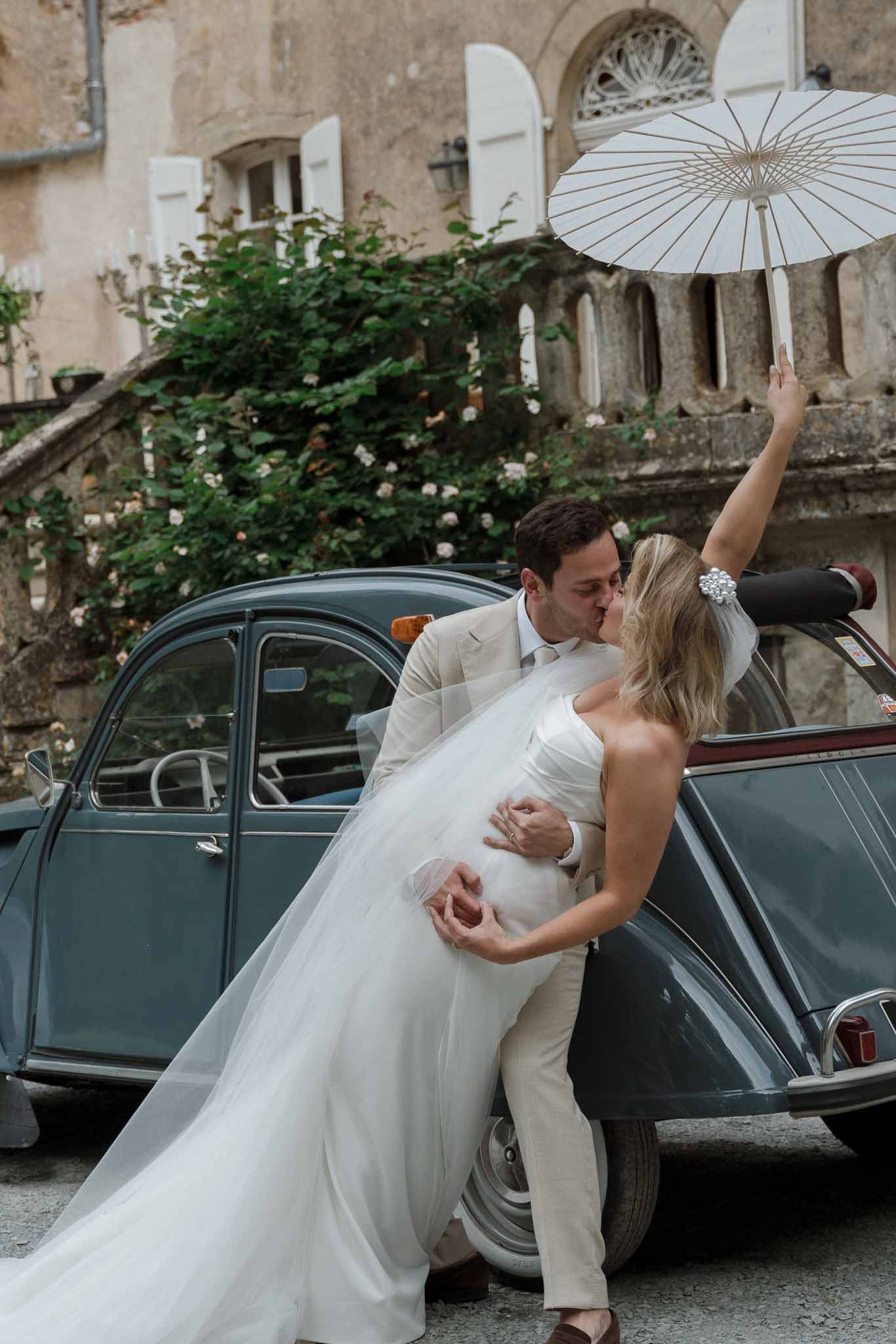 Groom carrying bride exiting vintage car at historic stone courtyard venue