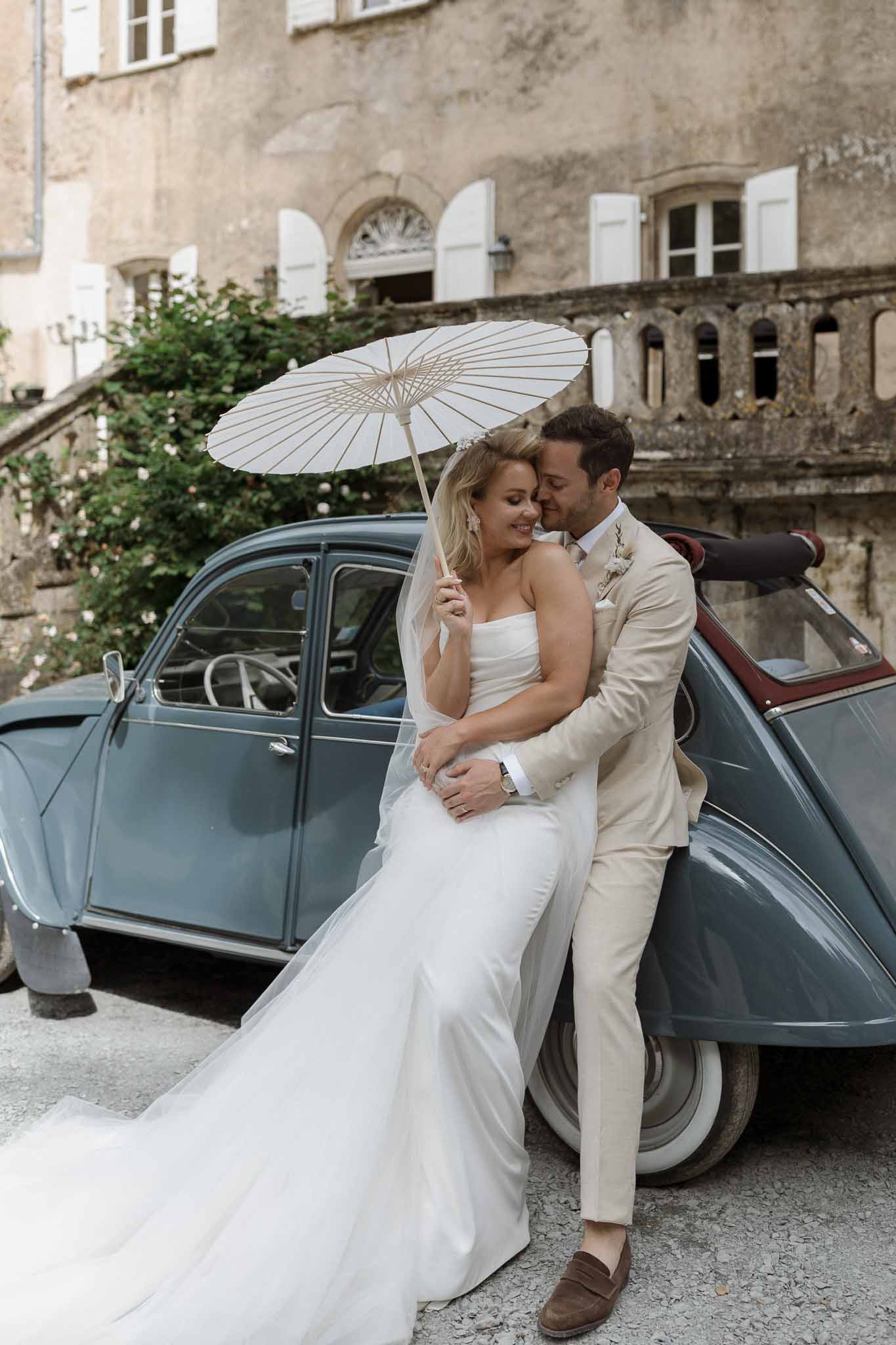 Bride and groom posing with vintage Citroën 2CV at stone château courtyard