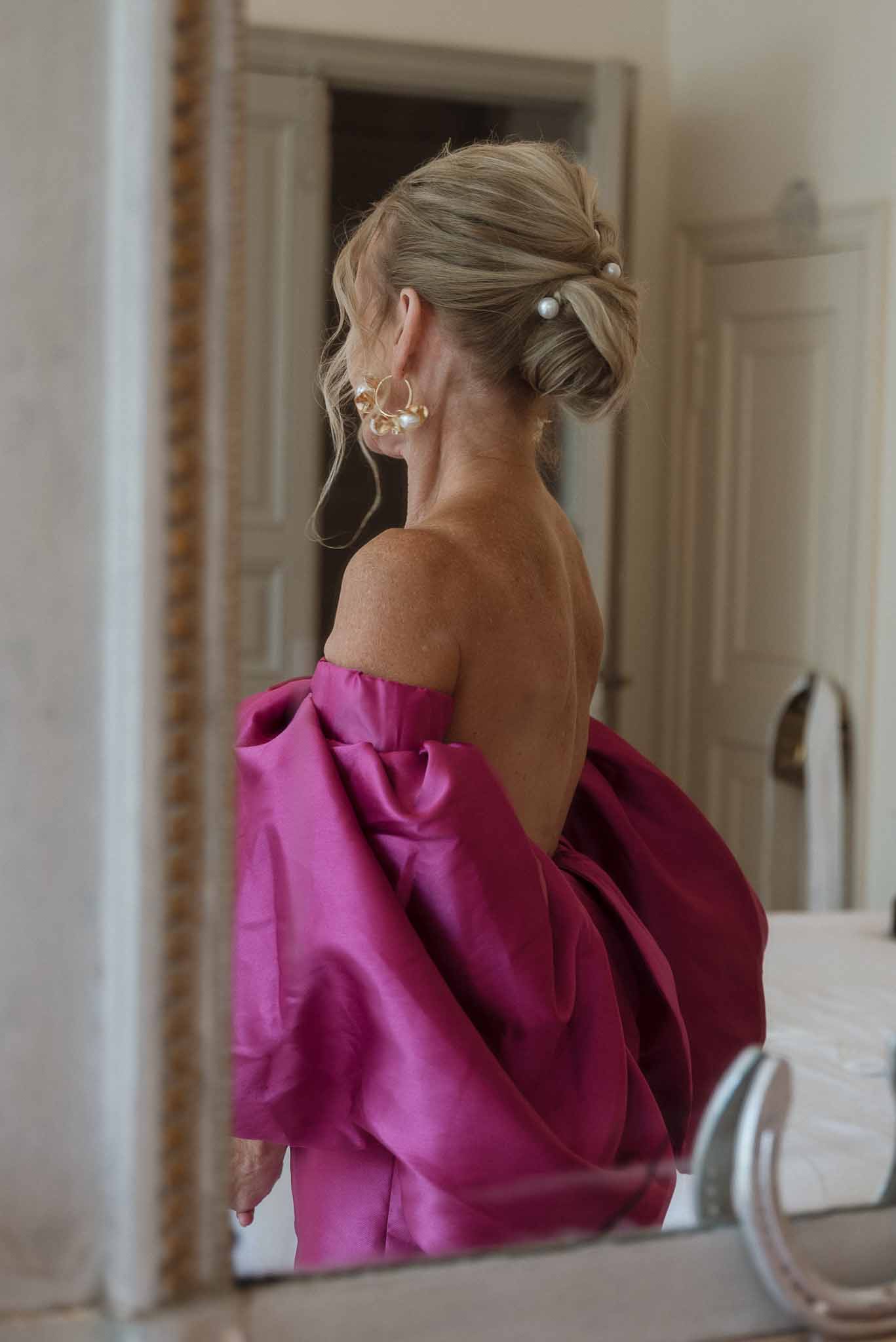 Wedding guest in magenta dress getting ready in indoor hallway mirror reflection