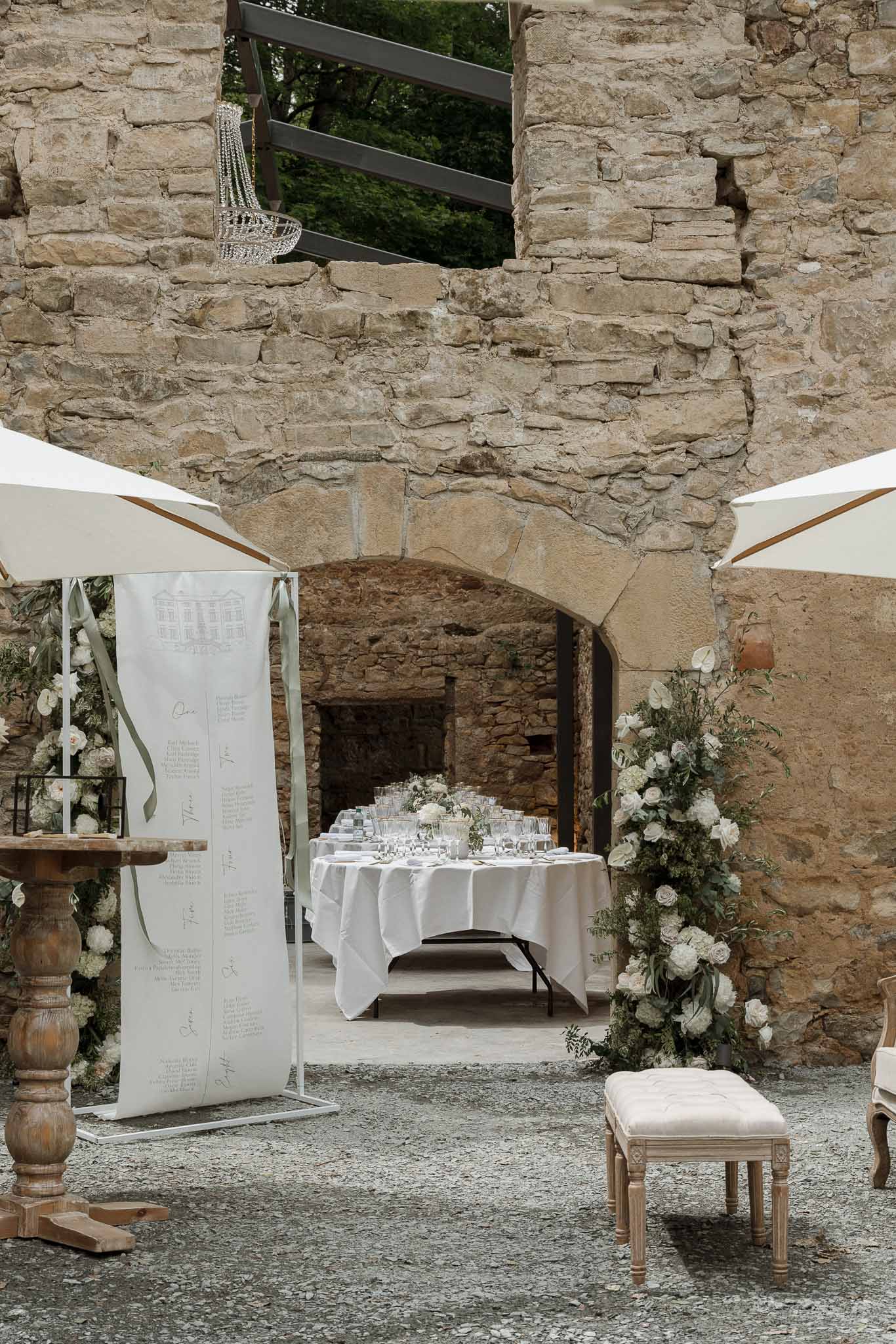 Historic stone courtyard reception setup with cream sails and white linens at wedding venue