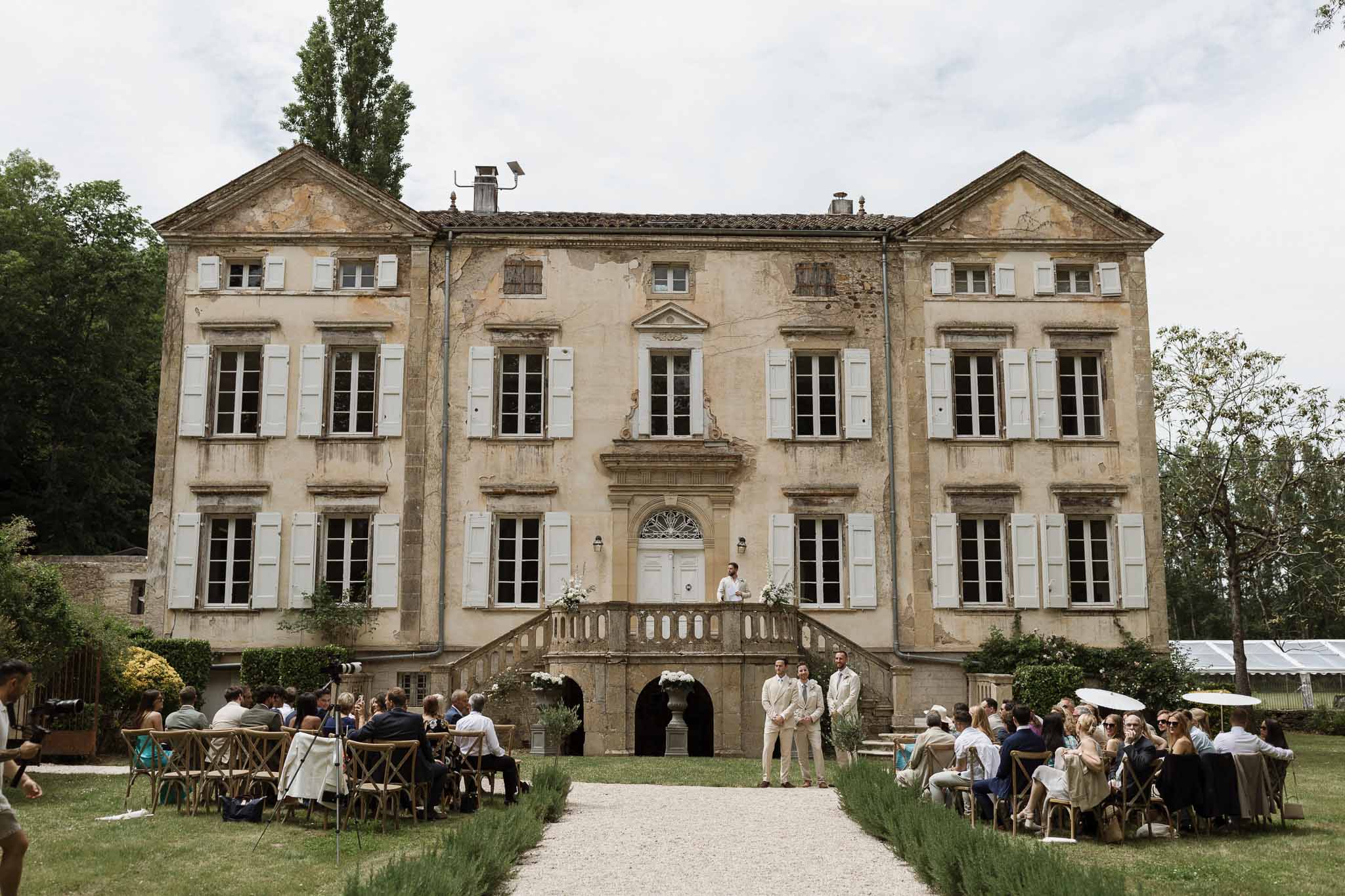 Outdoor wedding ceremony at 18th-century French stone manor house with guests seated on lawn