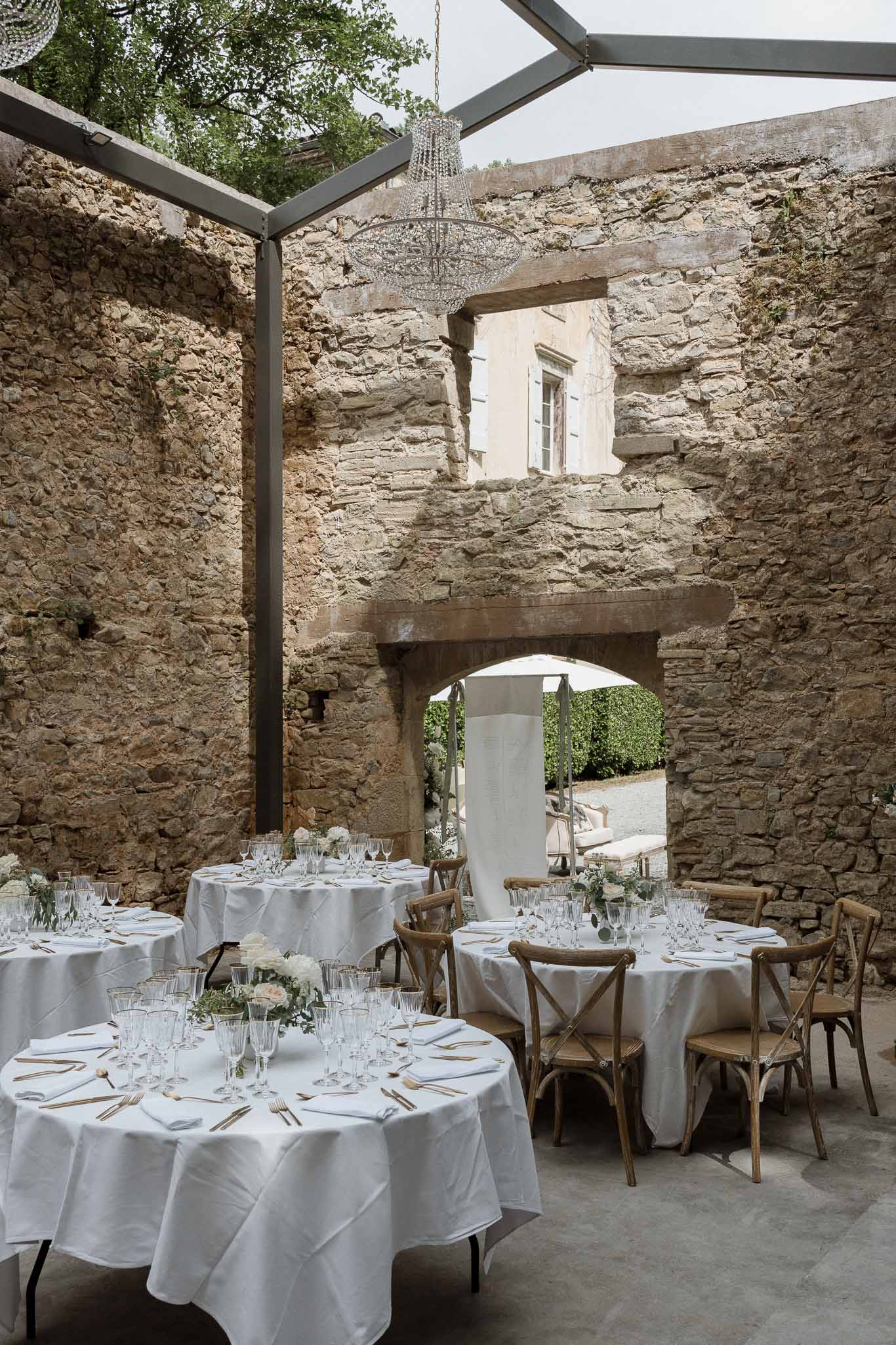 Reception setup in historic stone courtyard with round tables and crystal chandelier