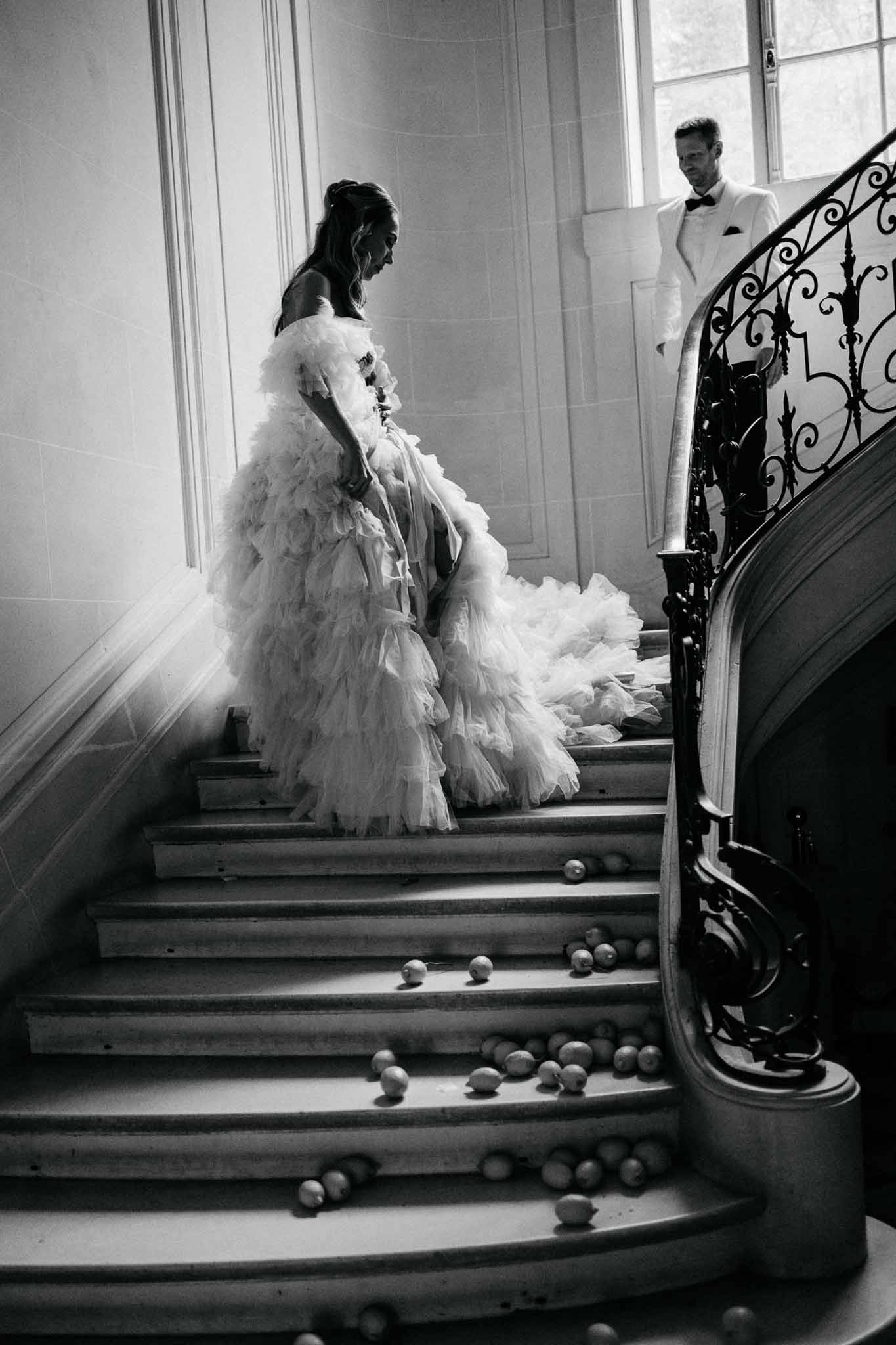 Bride ascending grand staircase while groom watches from above in elegant interior venue