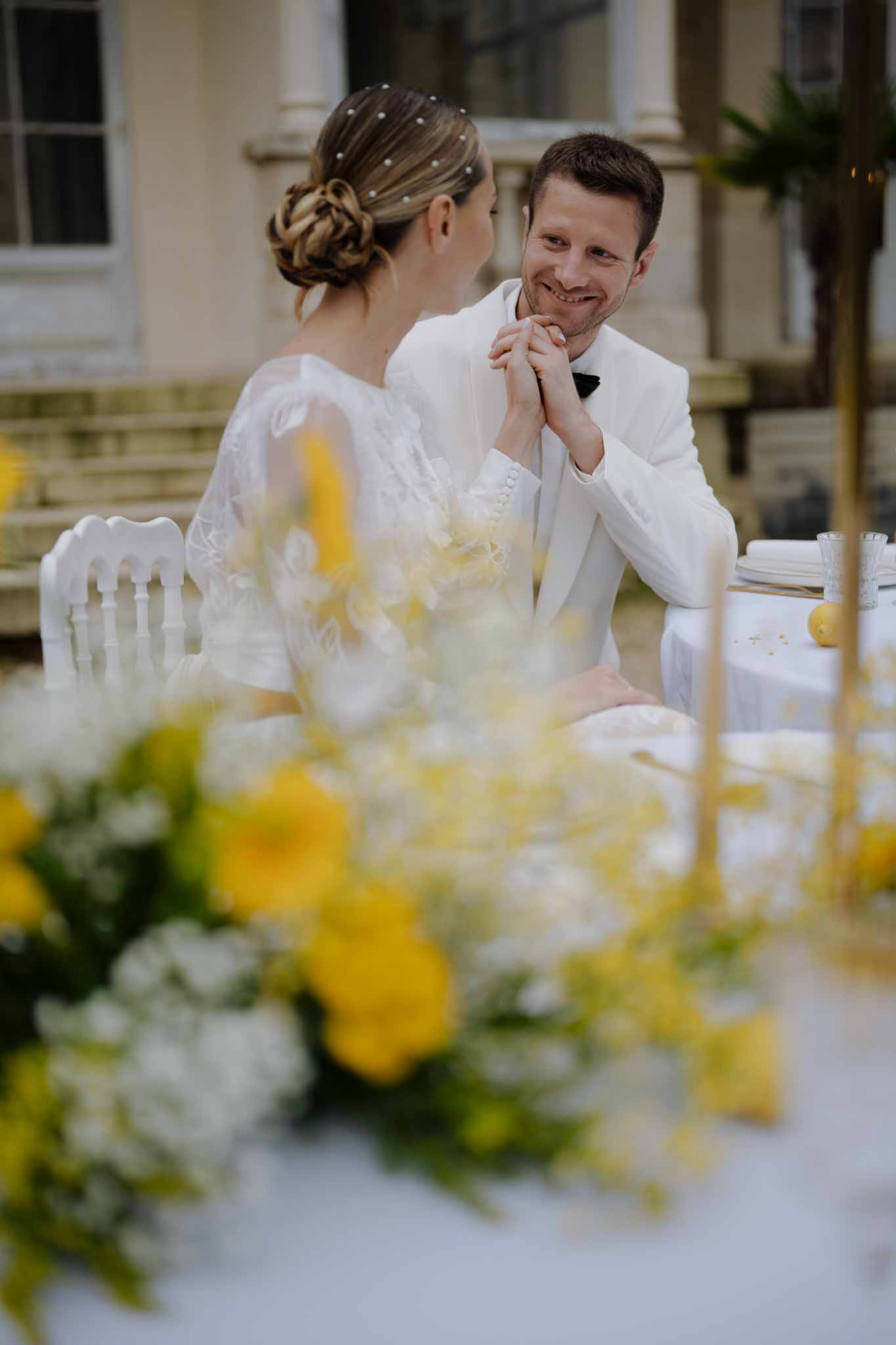 Bride and groom sharing intimate moment at reception table in courtyard setting with floral centerpieces