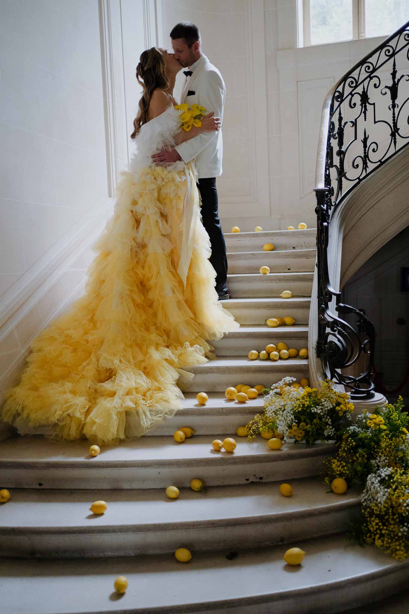 Bride and groom kissing on ornate staircase with yellow lemon and floral decor in elegant indoor venue