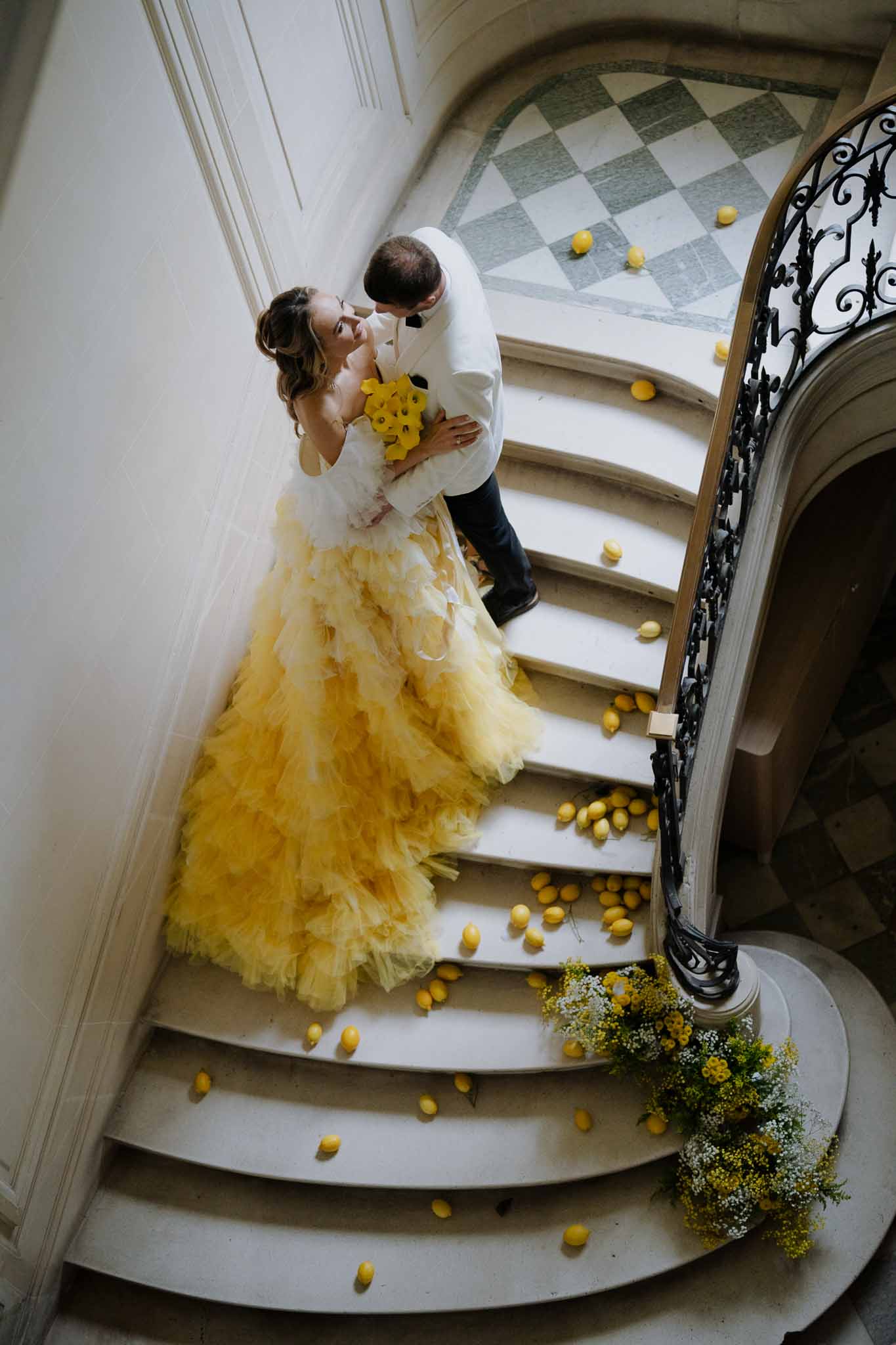 Aerial view of bride and groom kissing on ornate stone staircase with yellow florals at elegant wedding venue