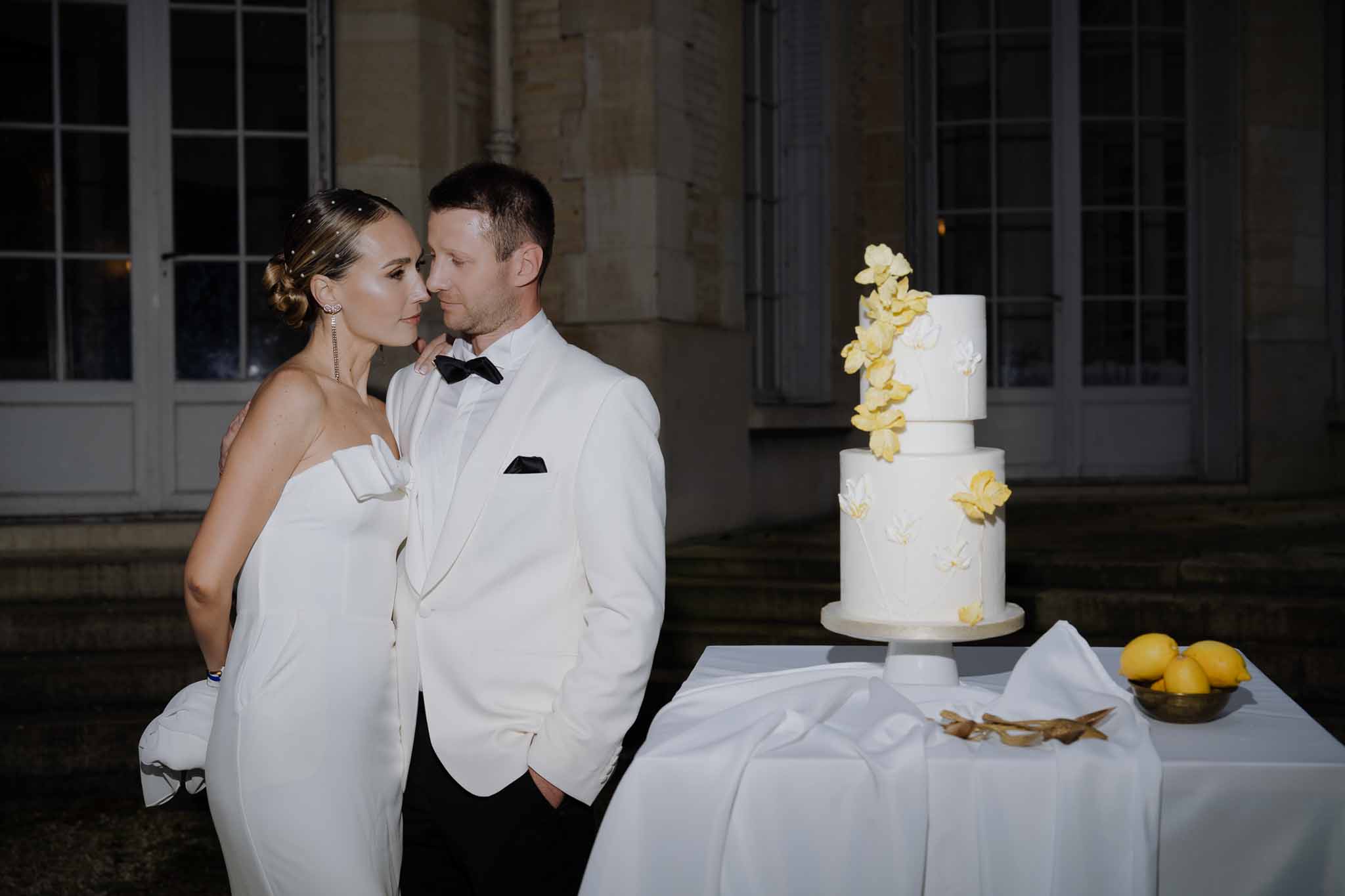 Bride and groom beside two-tier wedding cake with yellow orchids at indoor reception venue