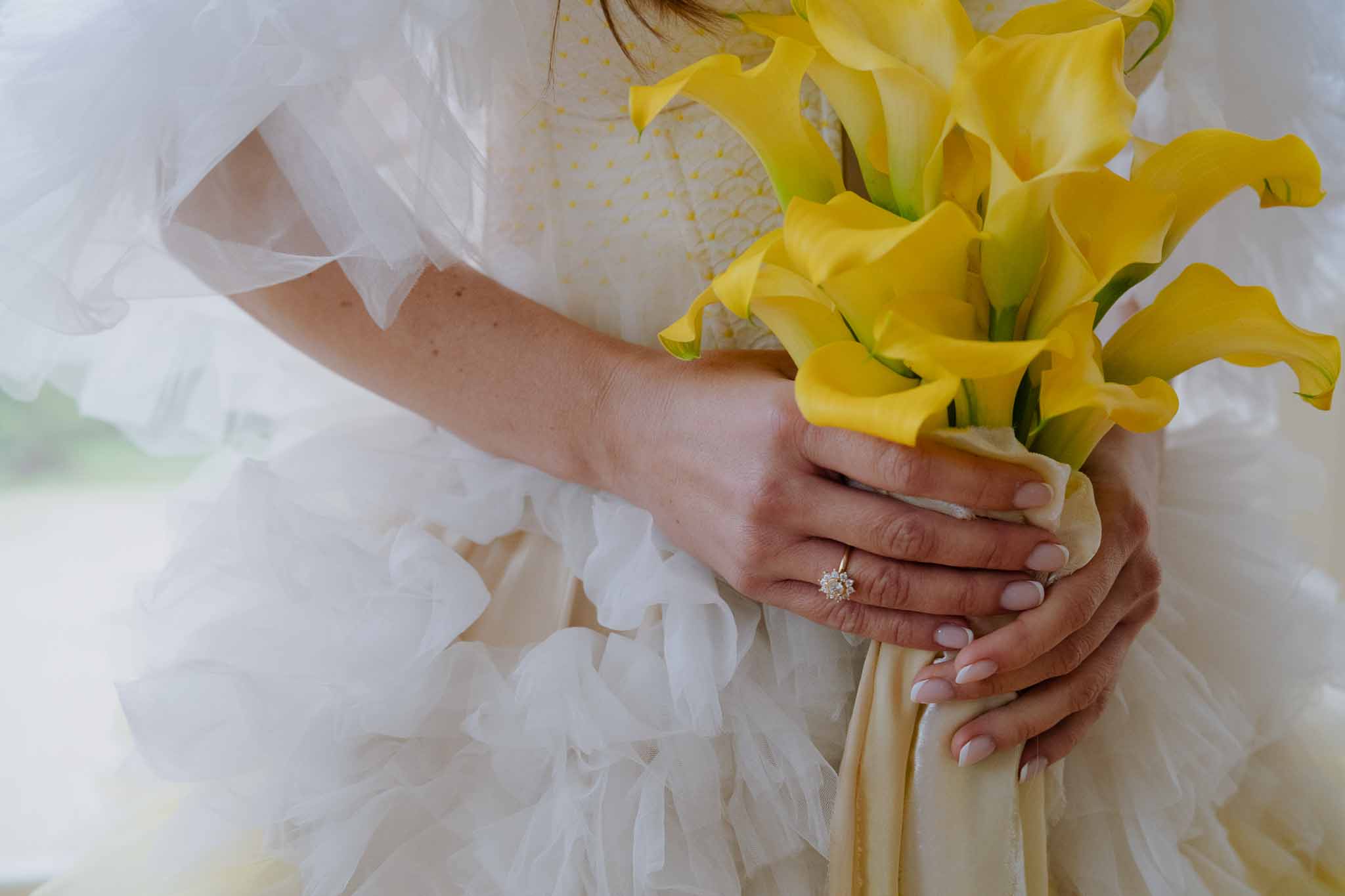 Bride holding yellow calla lily bouquet with ivory tulle dress and diamond engagement ring