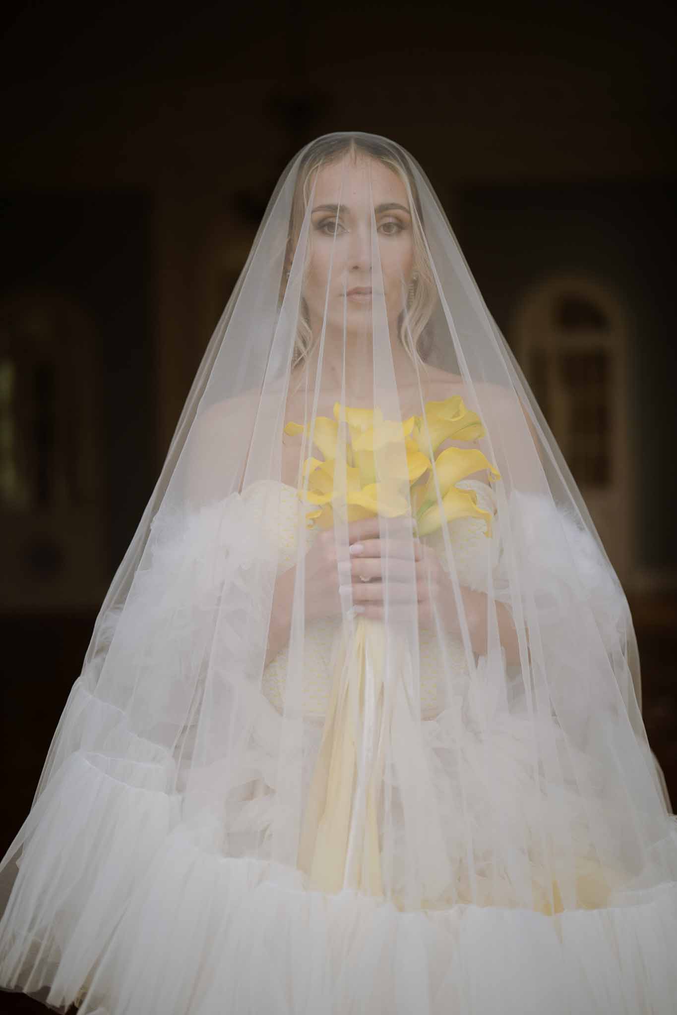 Bride in ivory veil holding yellow rose bouquet at indoor wedding venue