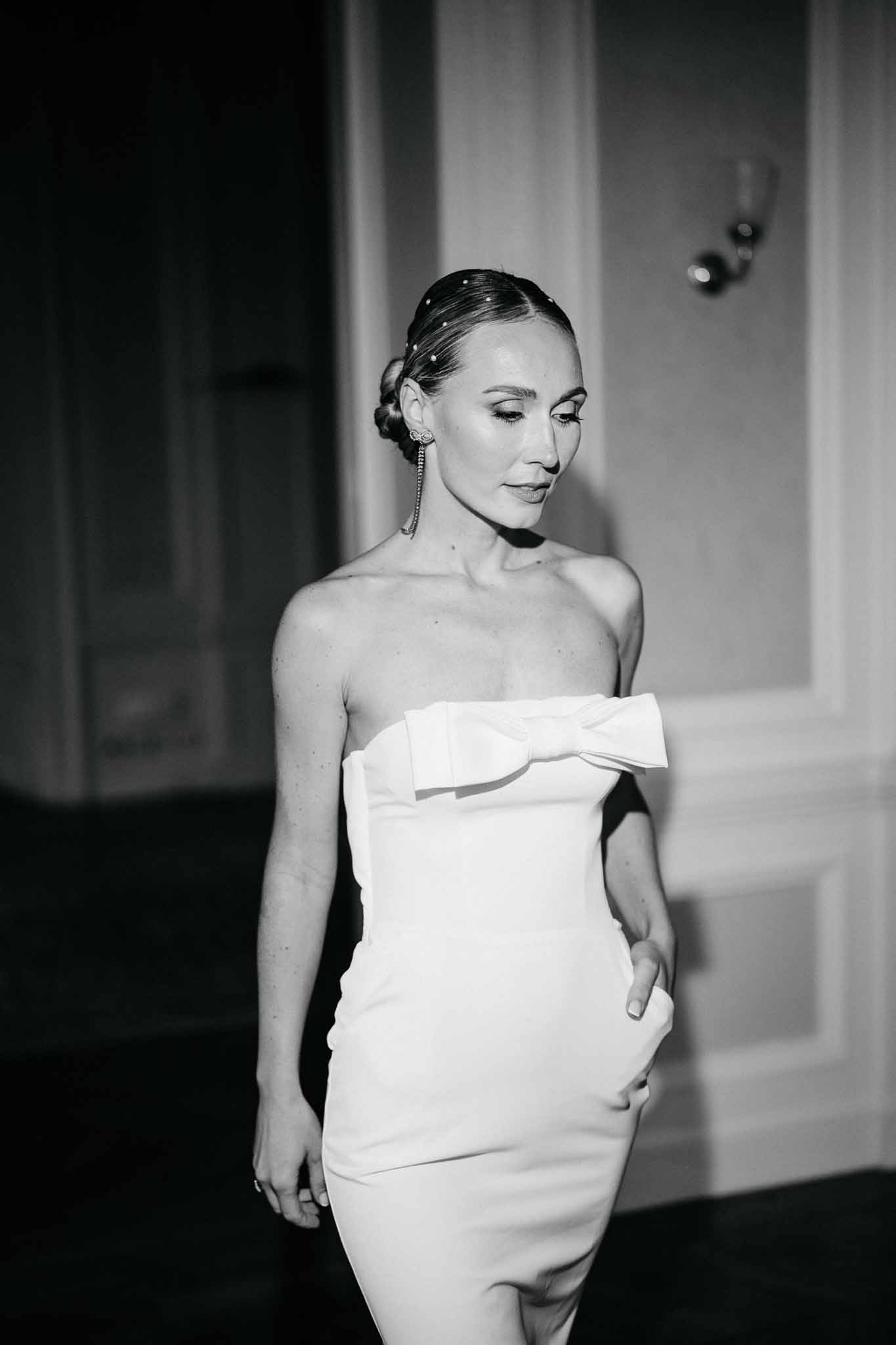 Black and white bridal portrait of bride in minimalist off-shoulder dress against neutral wall backdrop