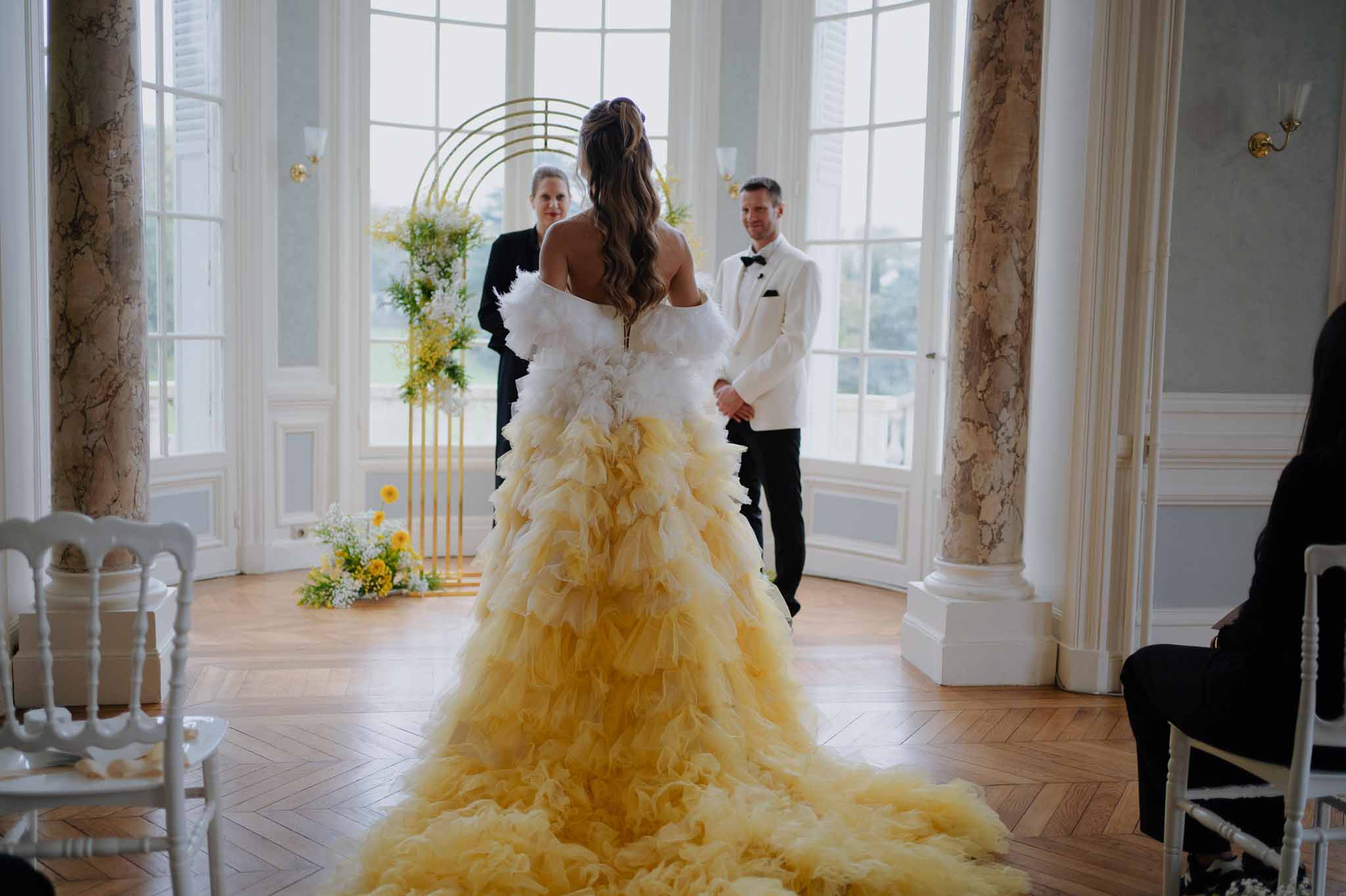 Bride walking down aisle during wedding ceremony in ornate ballroom with neoclassical architecture