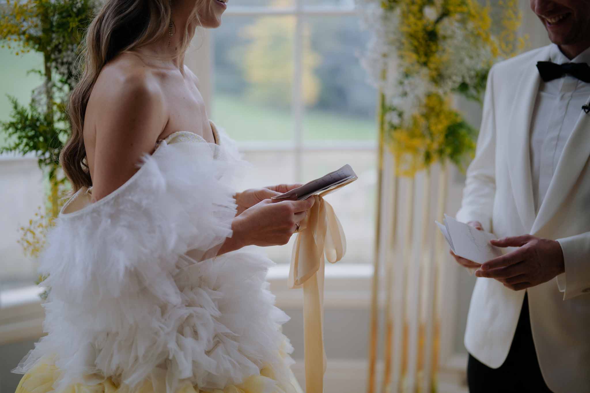 Bride and groom exchanging vows during indoor wedding ceremony with greenery and yellow flowers