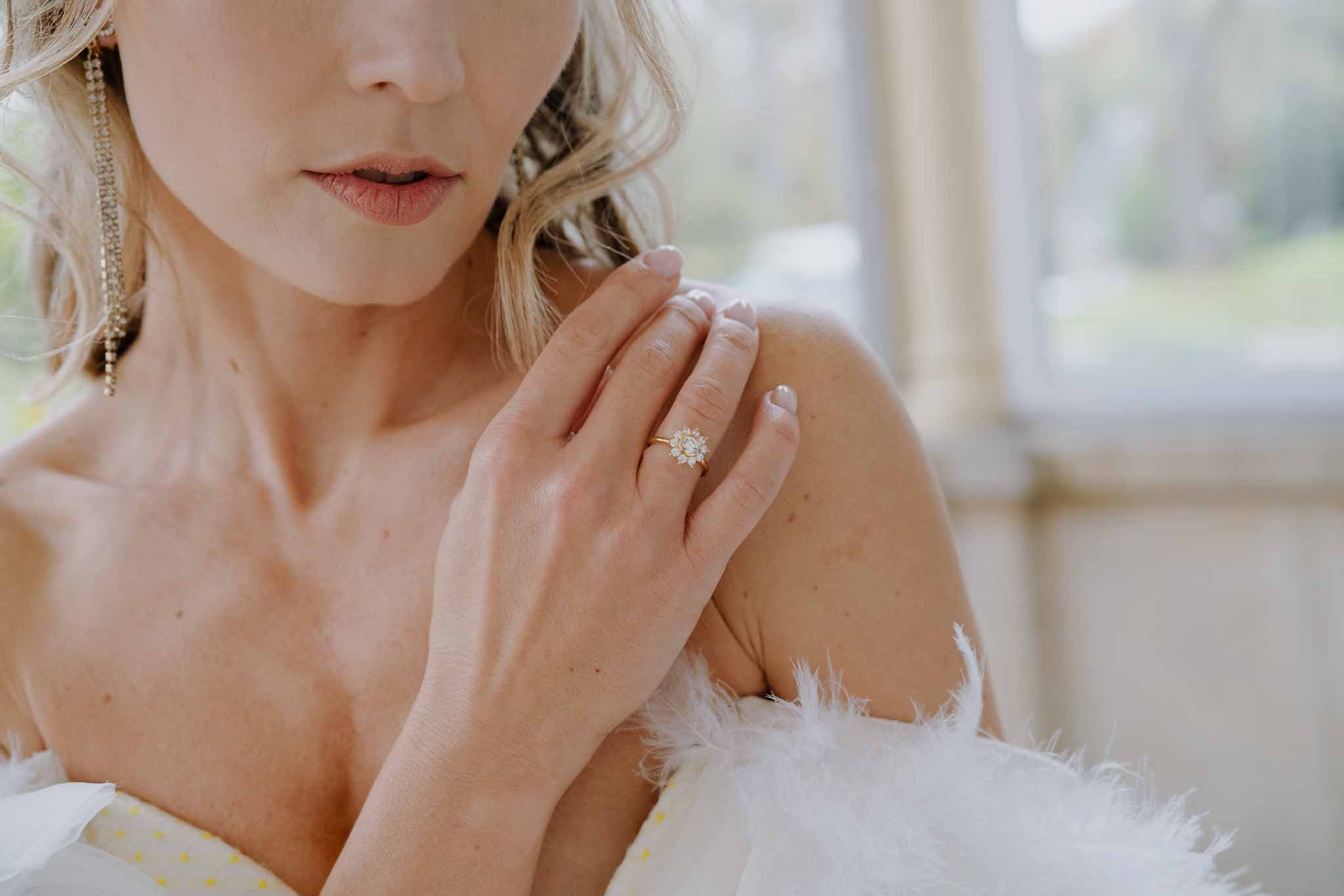 Bride showing engagement ring and wedding band in close-up portrait with pearl earrings and feathered gown details