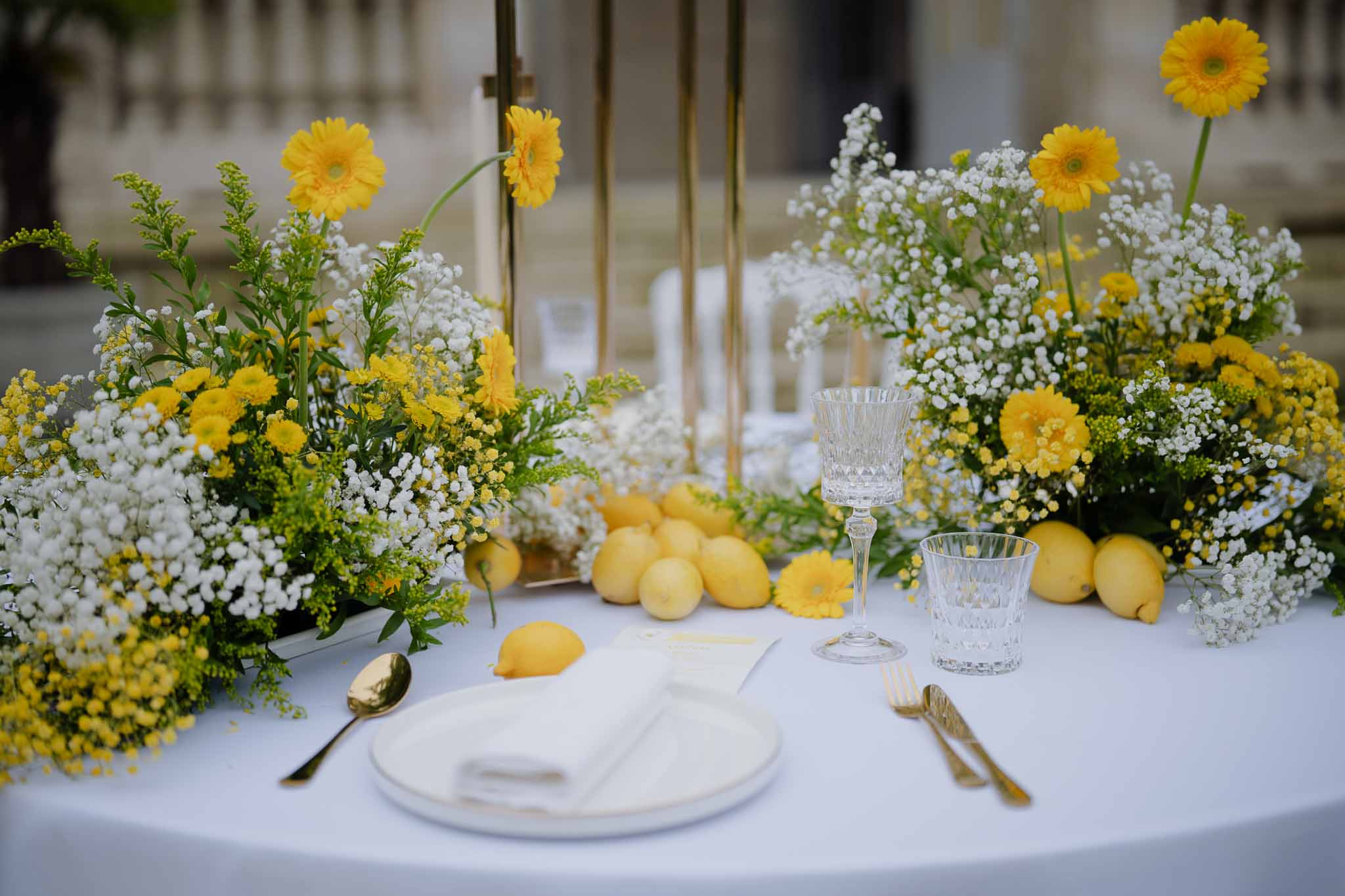 Yellow and white reception table setting with gerbera daisies and gold flatware at indoor wedding venue