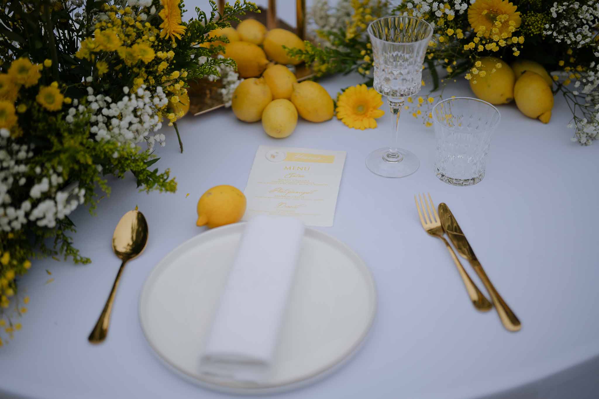 Yellow and white reception table setting with lemons and gerbera daisies at Mediterranean wedding