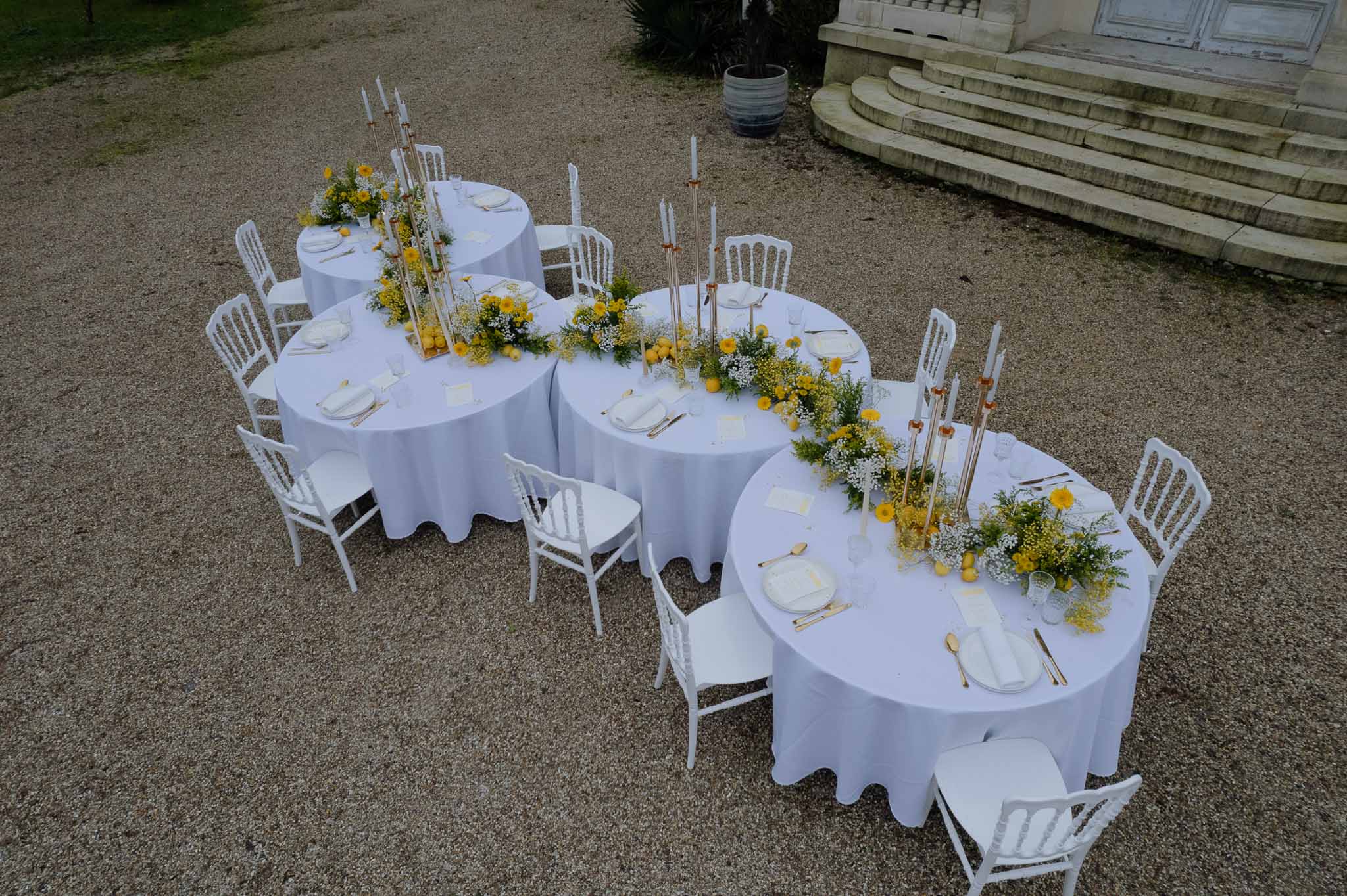 Aerial view of outdoor reception tables with white linens and gold accents at stone mansion courtyard