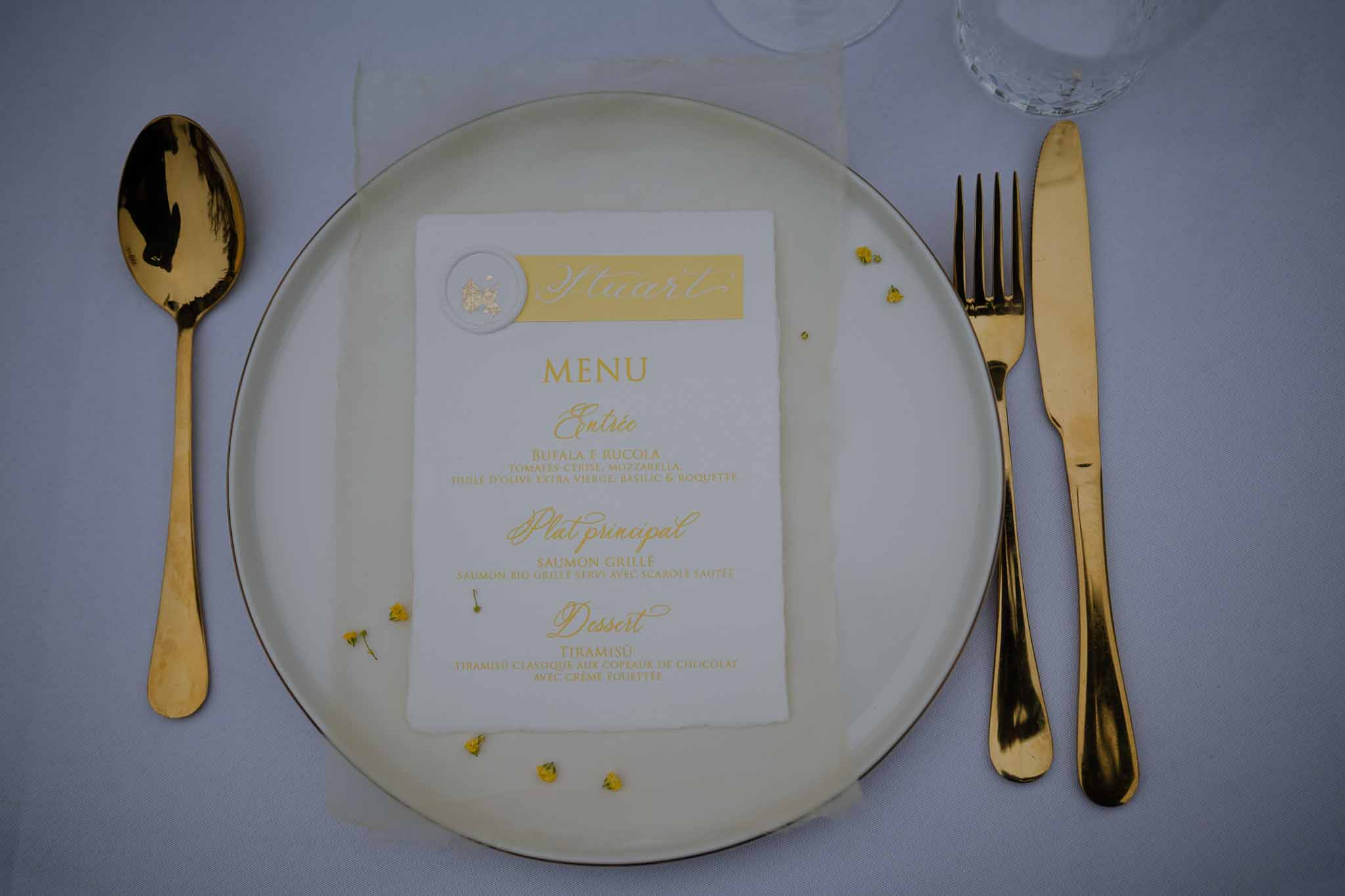 Elegant place setting with gold menu card and cutlery at formal wedding reception