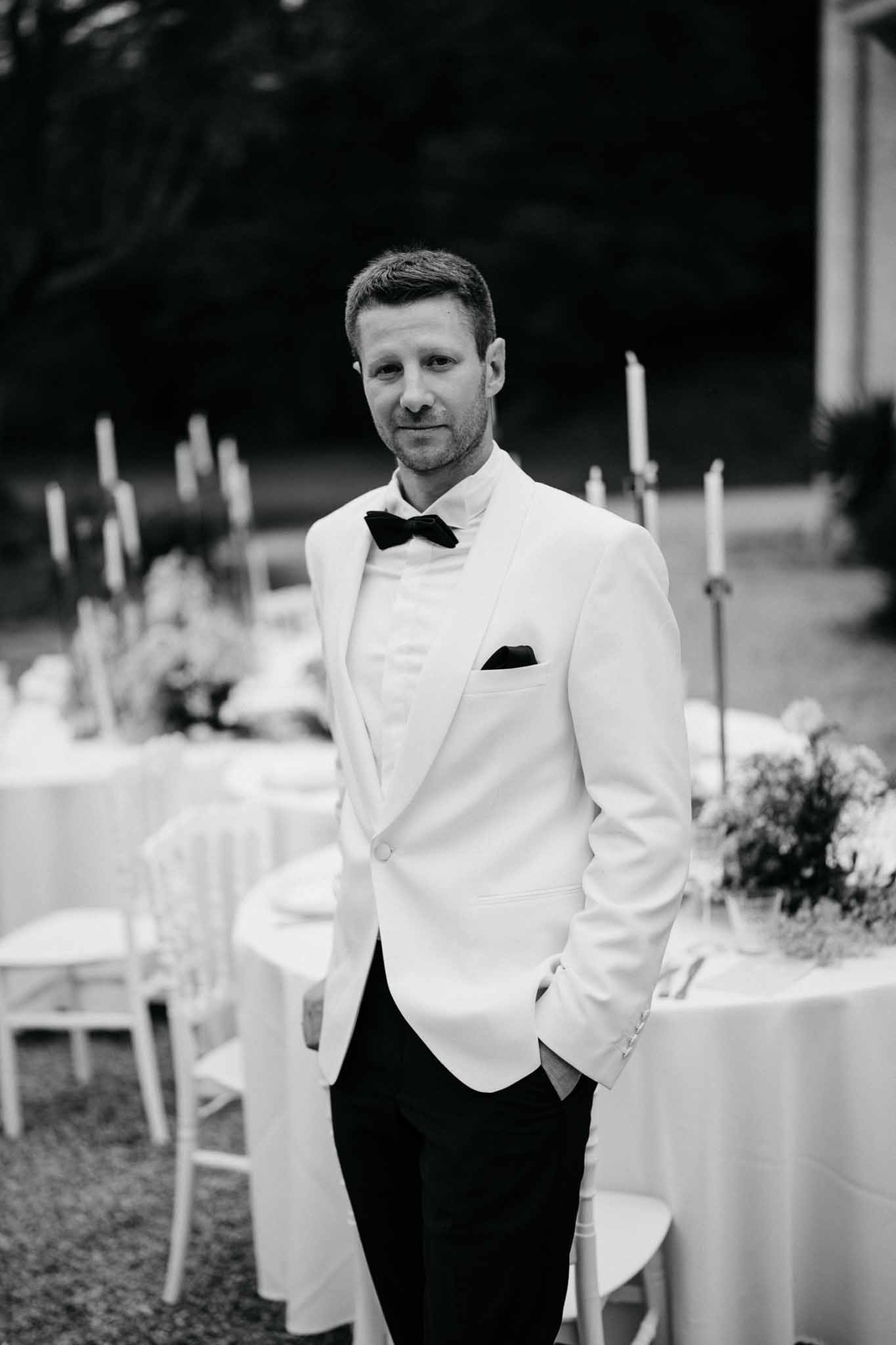 Groom in black-tie attire at outdoor reception venue with decorated dining tables