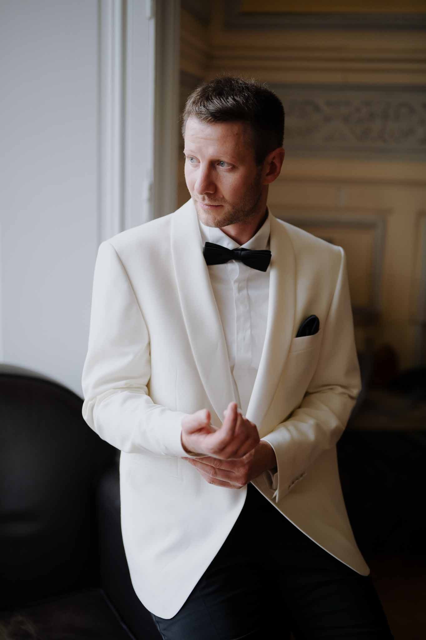 Groom in cream dinner jacket and bow tie portrait in elegant interior space
