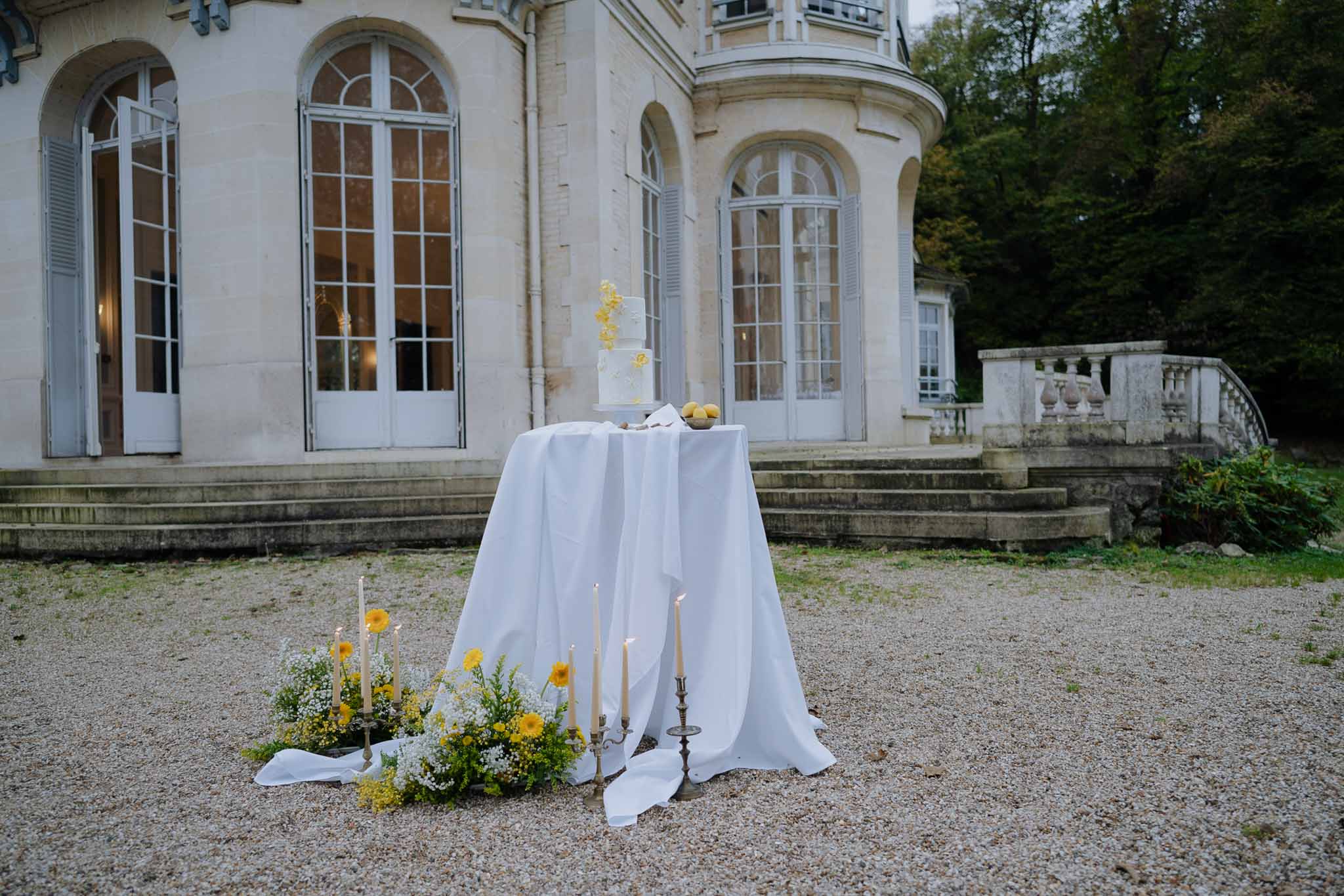 Cocktail hour table setup in courtyard of classical stone manor house with yellow flowers and candles