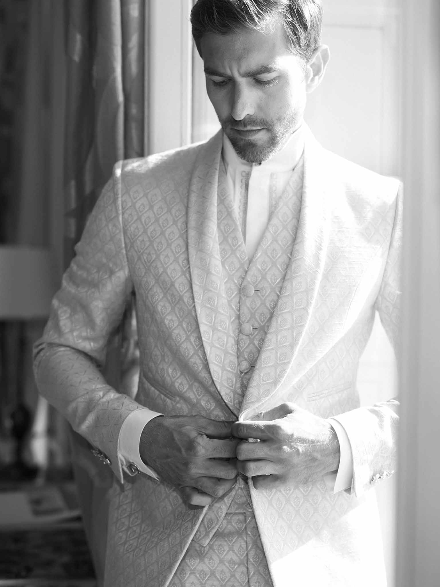 Groom adjusting his three-piece suit during wedding preparations in indoor setting