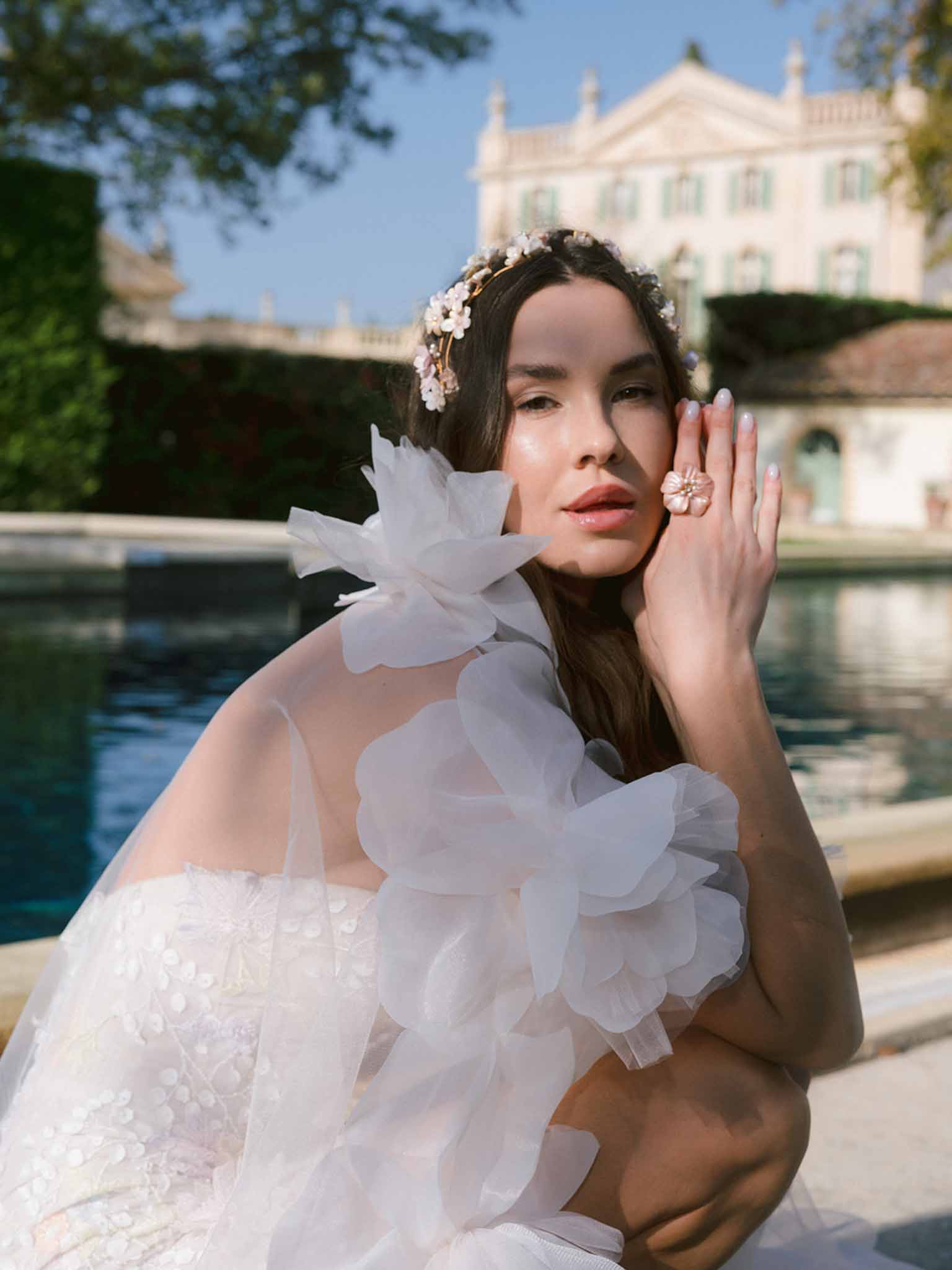 Bride in ivory tulle wedding dress with floral crown by pool at neoclassical estate
